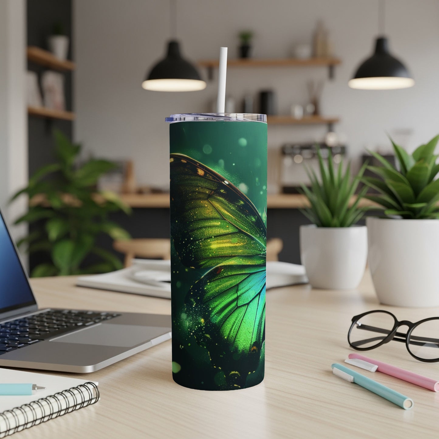 Green butterfly wing tumbler with straw on a desk.