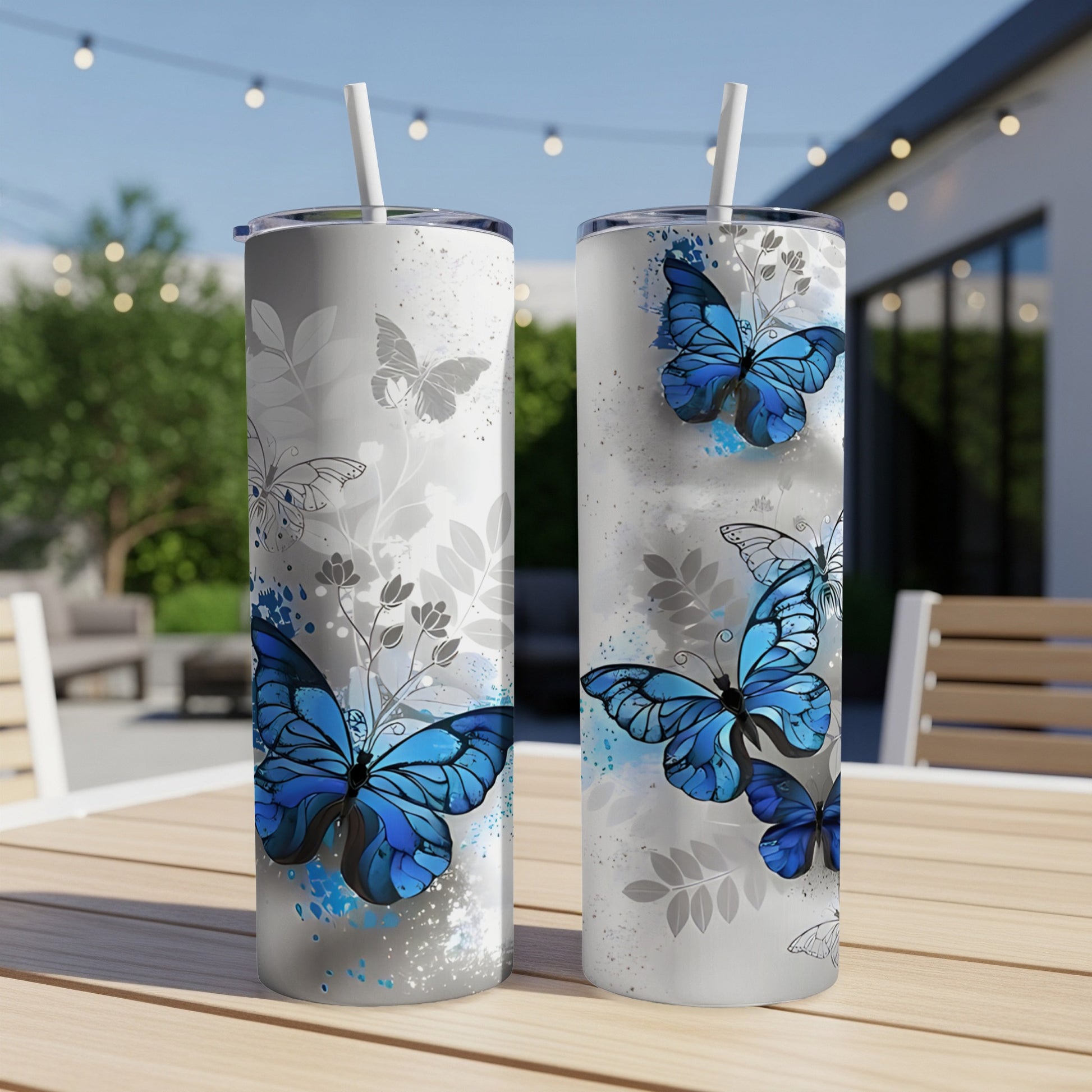 Two tumblers with blue butterflies and grey floral patterns on a patio table.