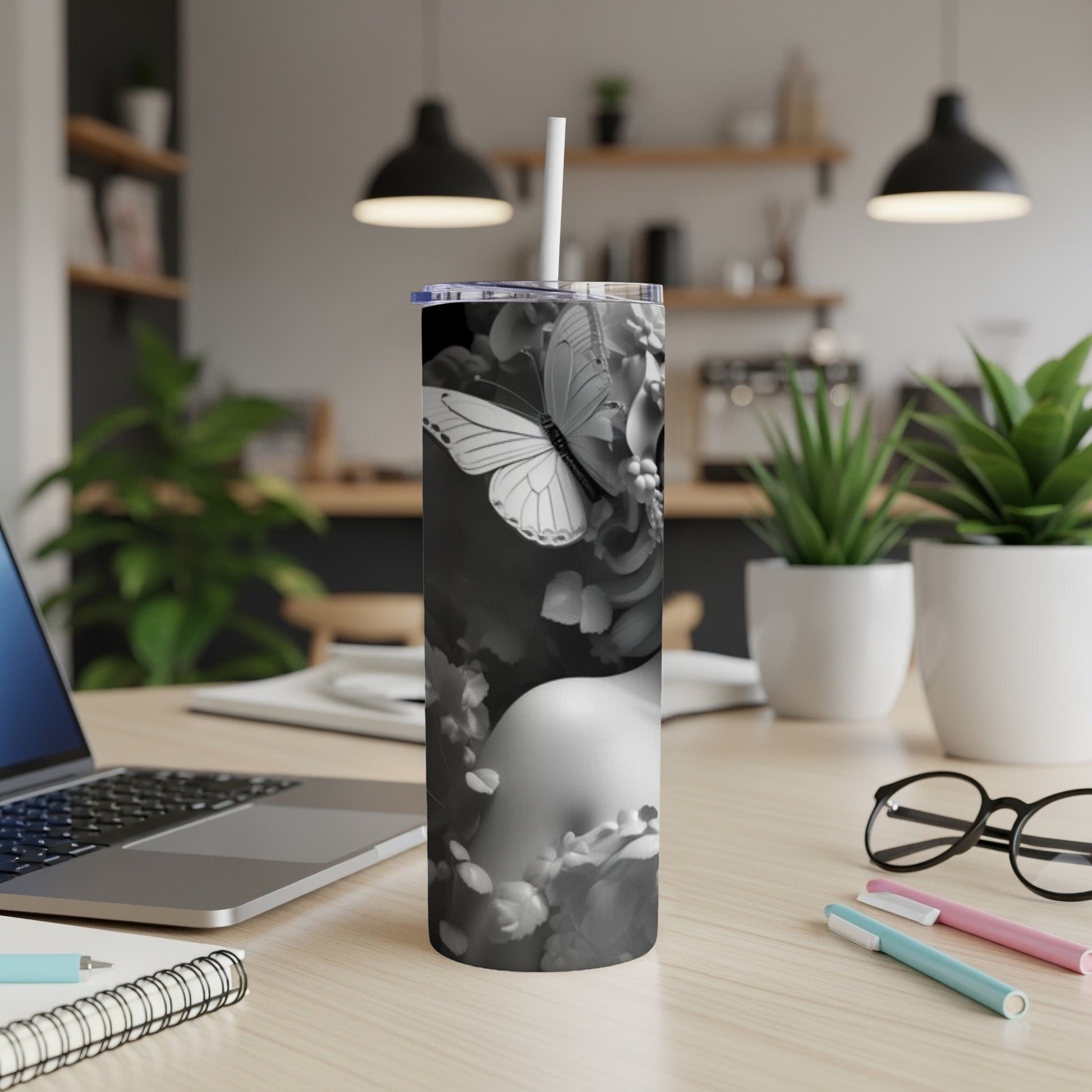 Black and white tumbler with butterfly and floral design, next to laptop.