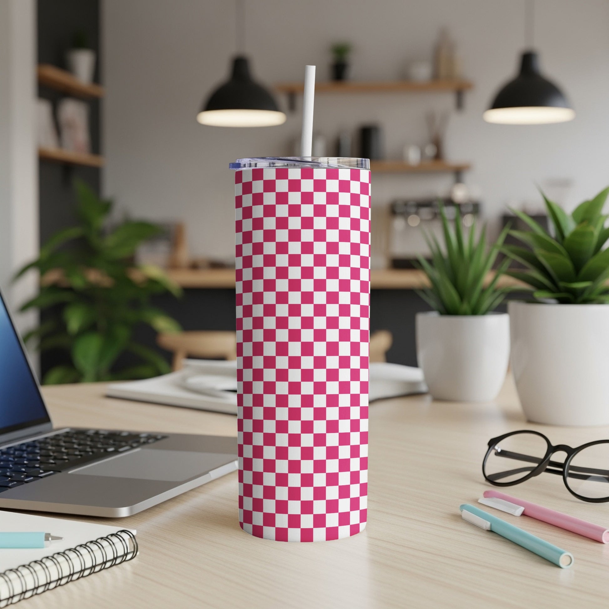 Pink and white checkered tumbler with straw on a desk.