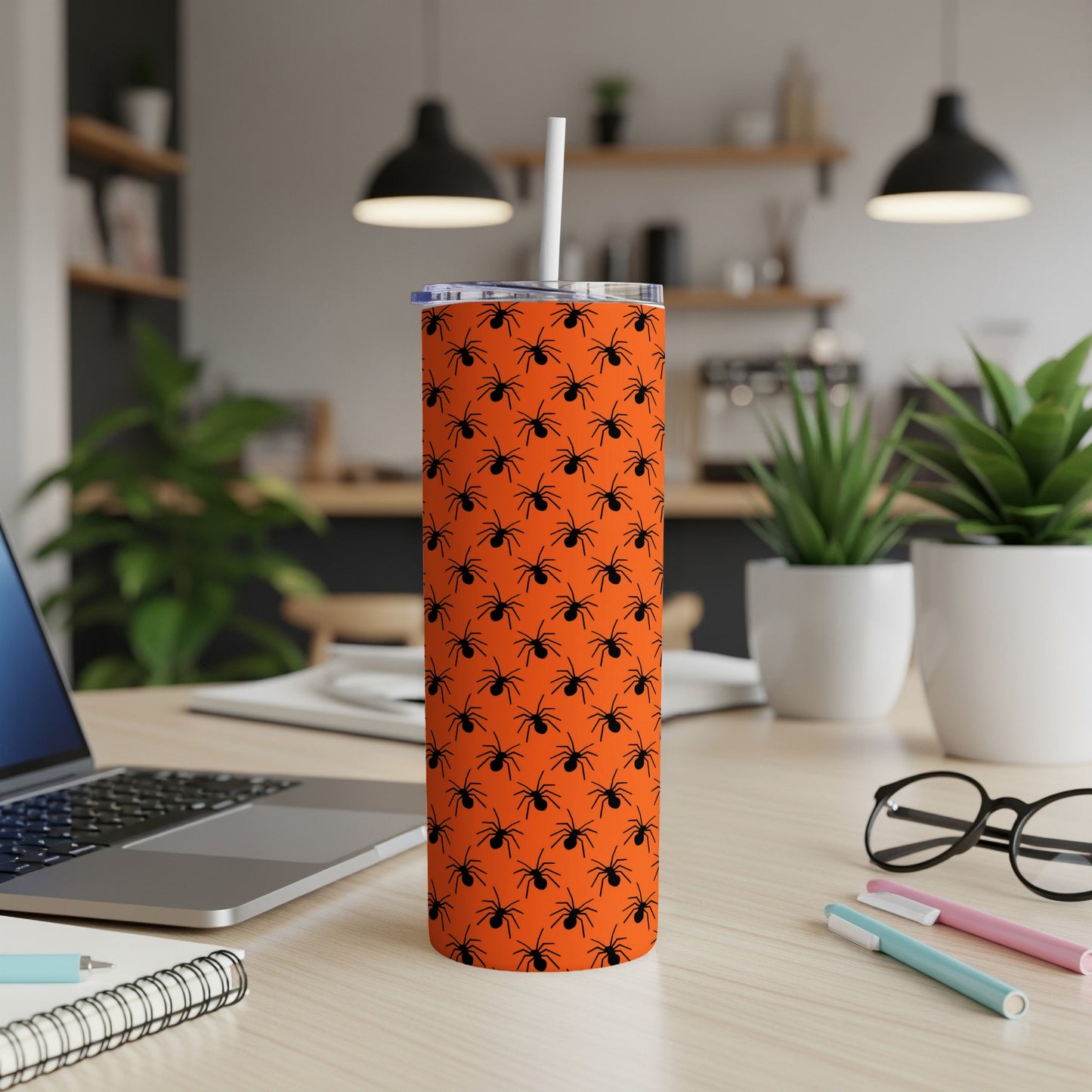 Orange tumbler with a black spider pattern and white straw on a desk.