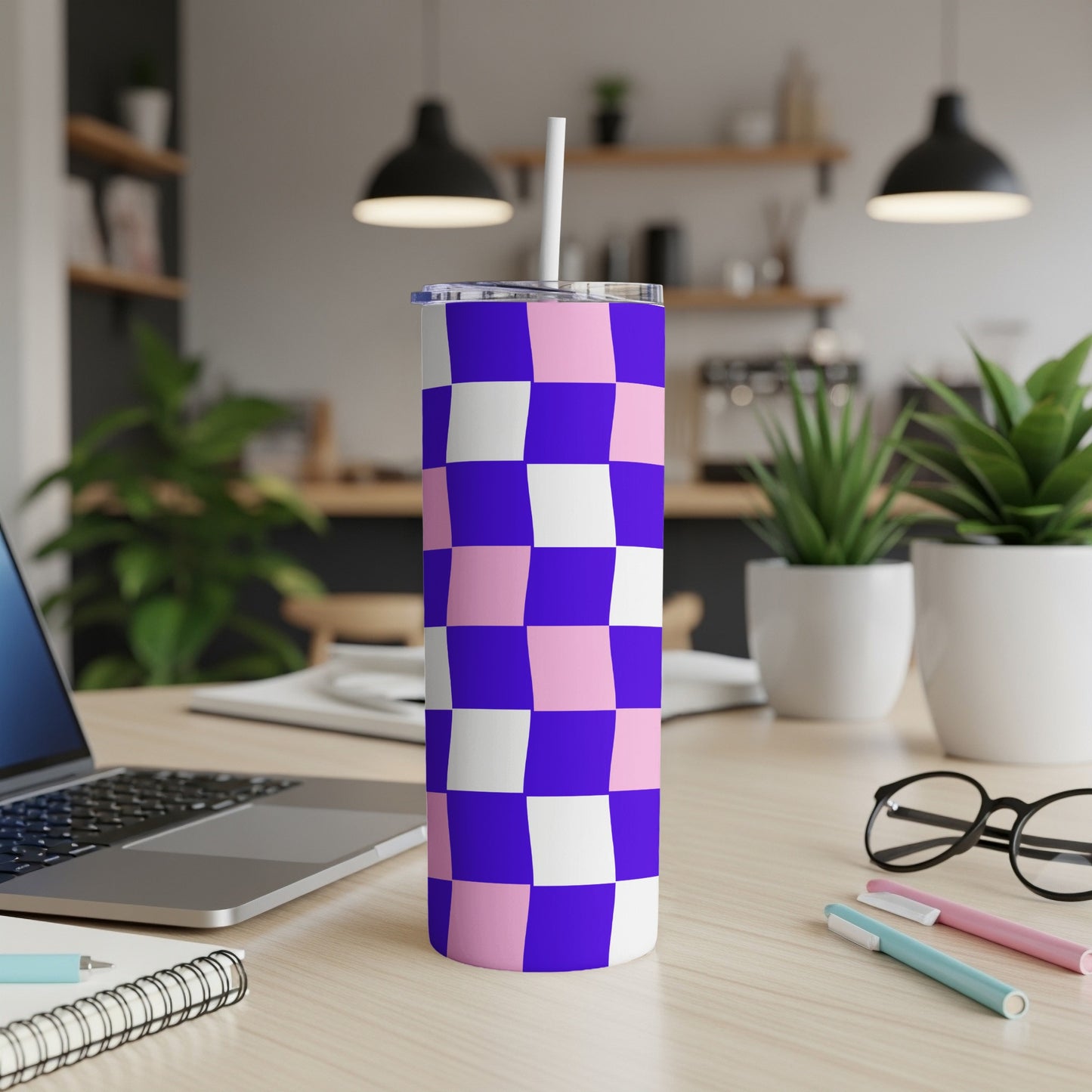 Purple and pink checkerboard tumbler with straw on a desk.
