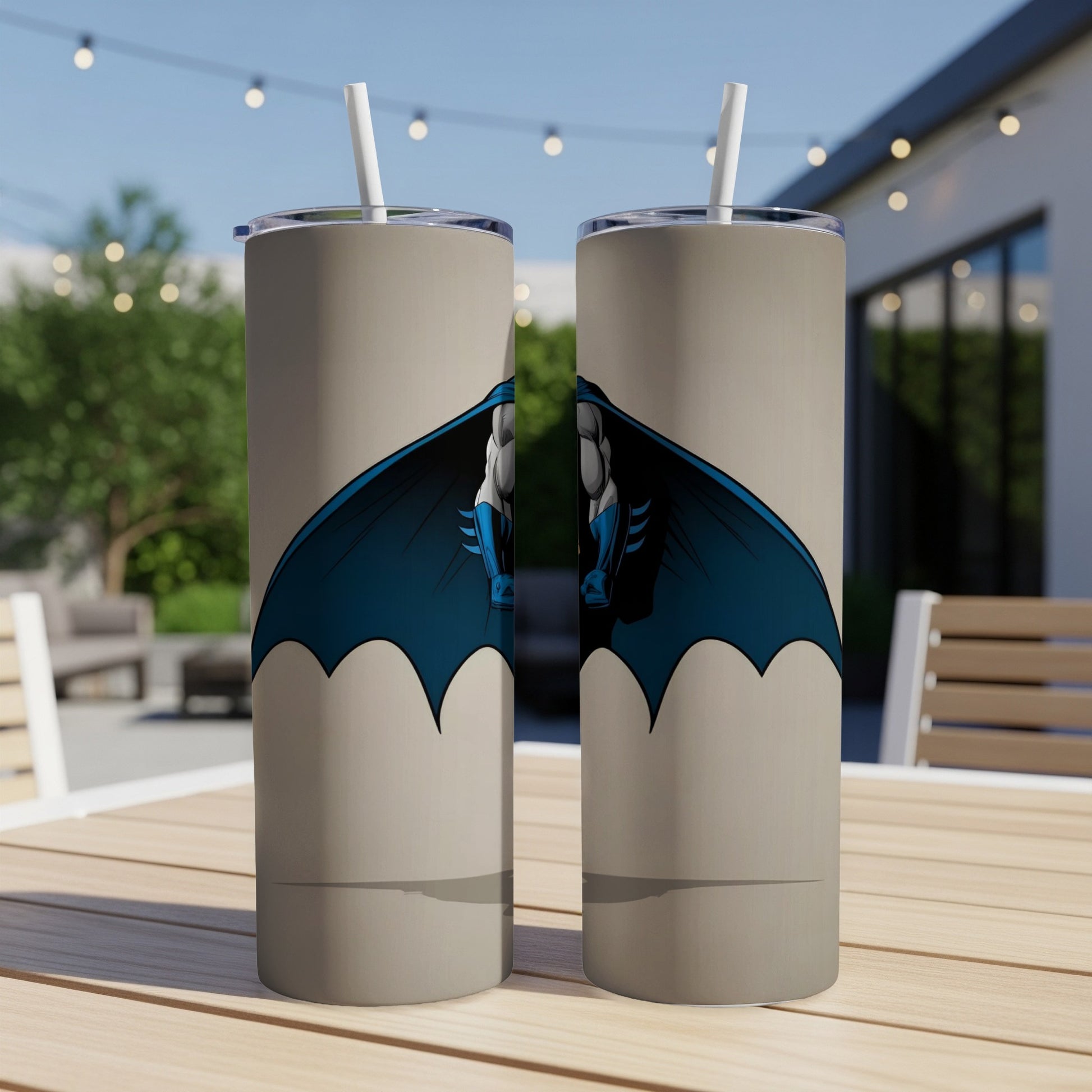 Two Batman tumblers with straws stand on a table outdoors.