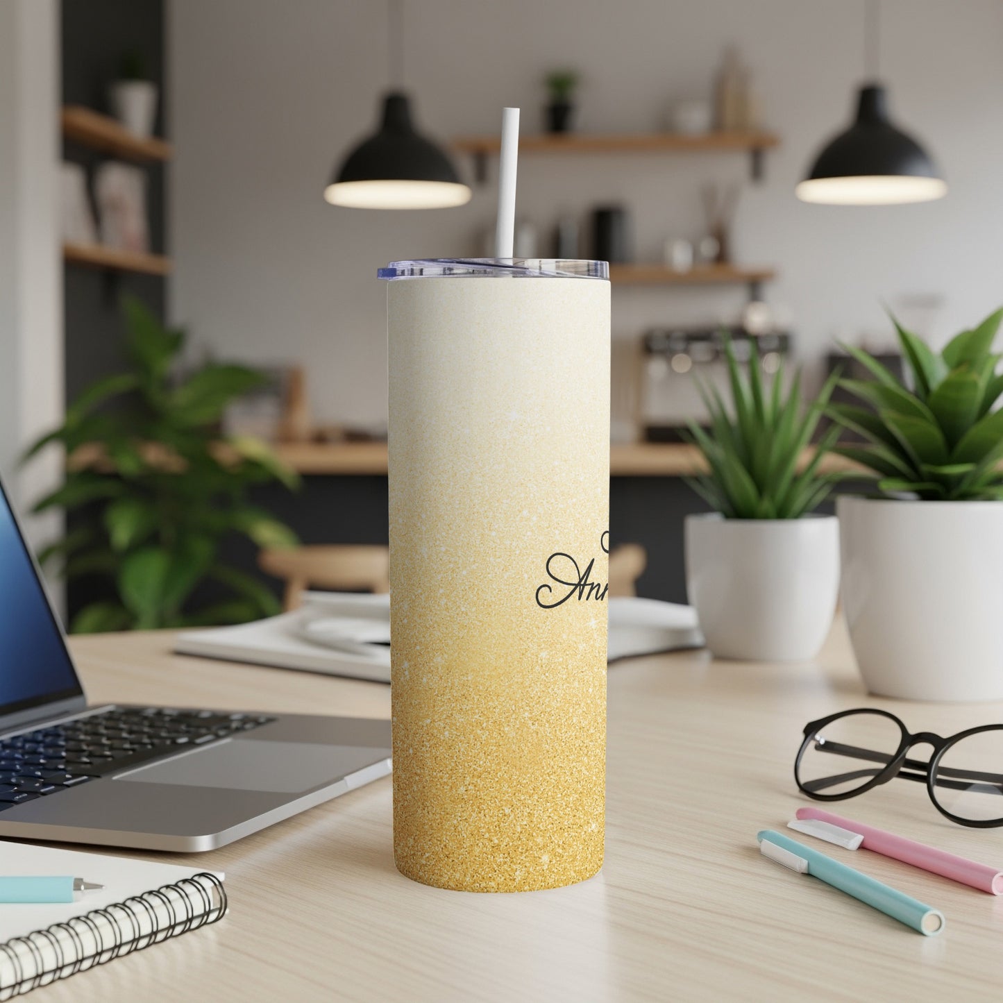 Gold glitter tumbler with straw and "Anniversary" text on desk.