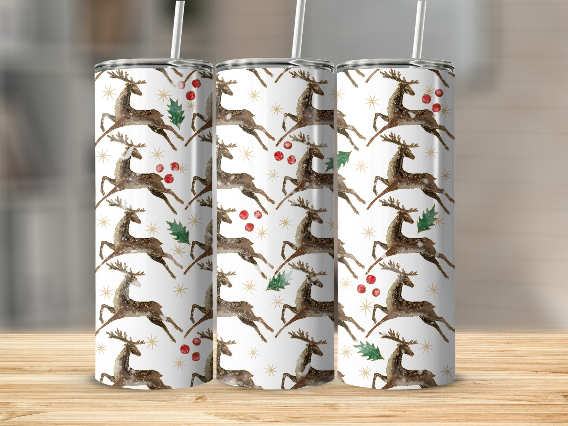 Reindeer pattern on three white tumblers with straws on a wooden surface.