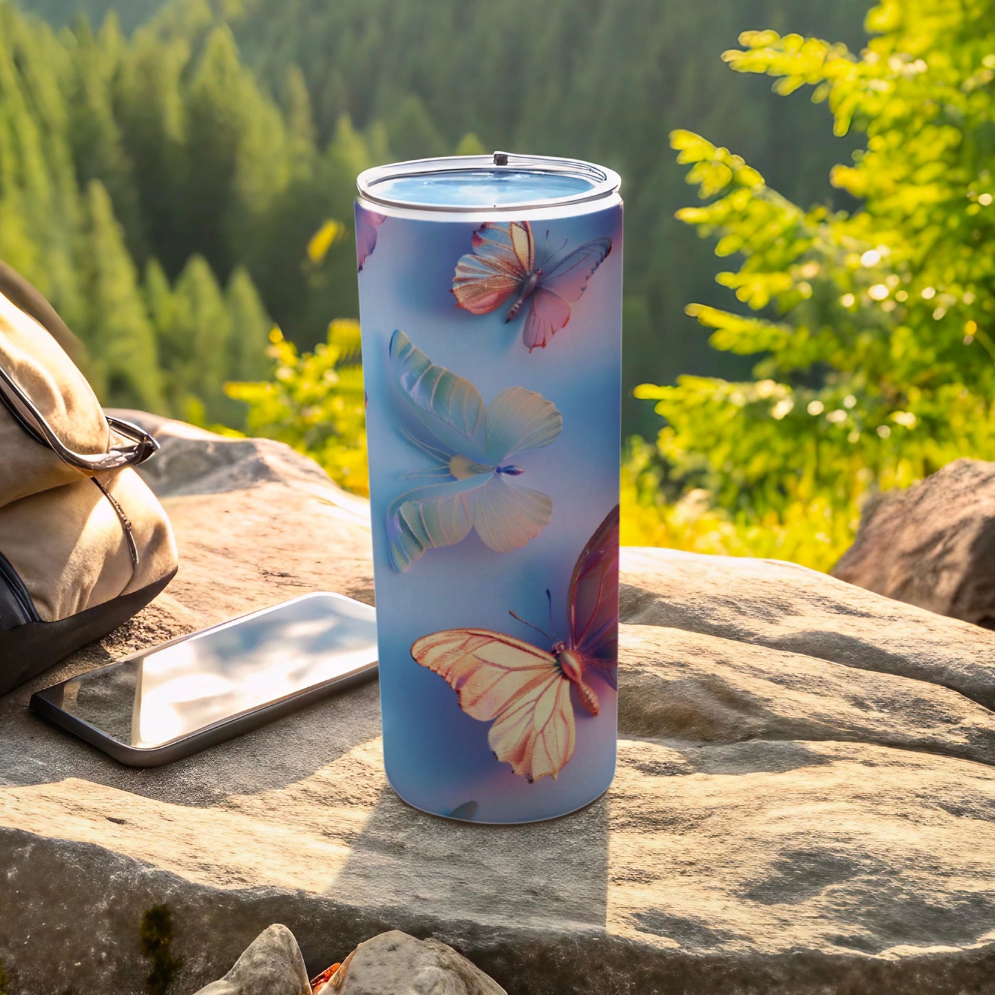 Blue tumbler with butterflies, a phone, and a backpack on rocks.