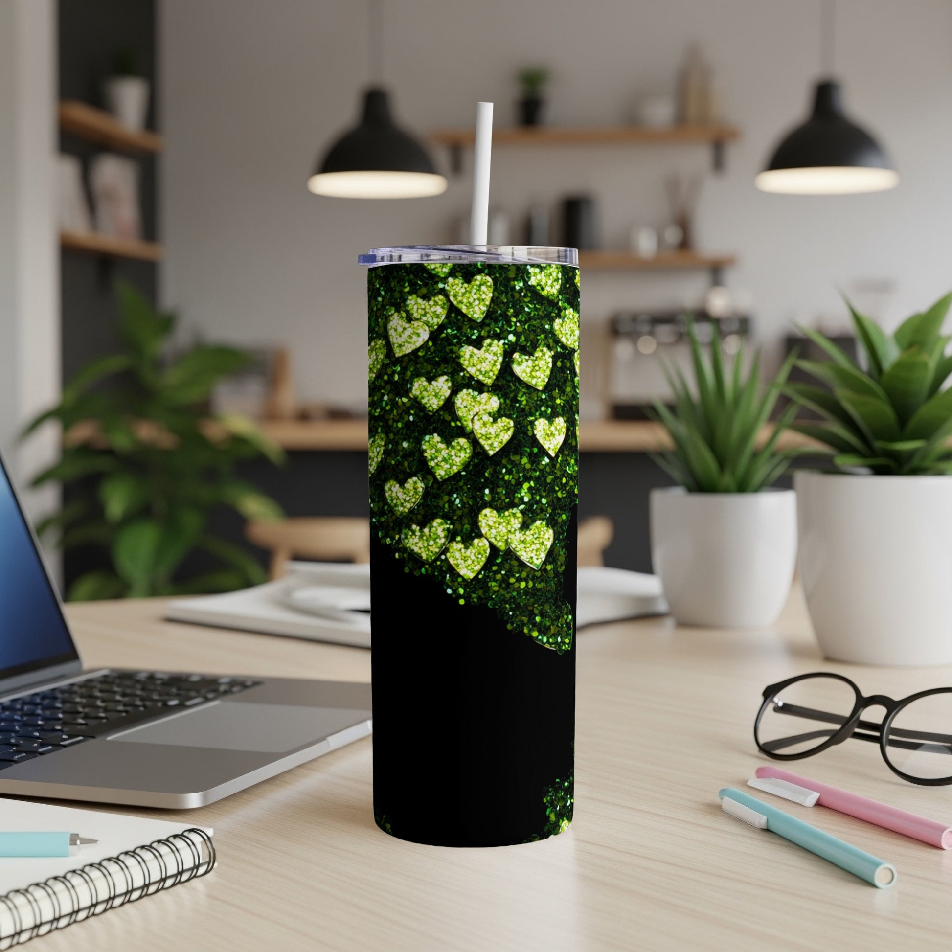 Black tumbler with green glitter hearts, on a desk with a laptop.