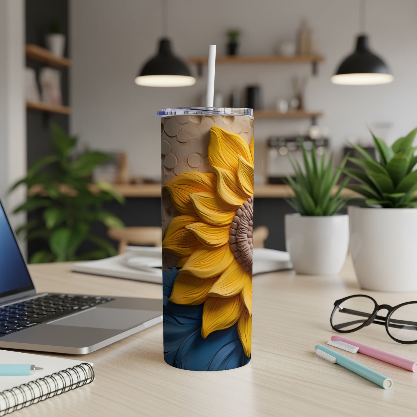 Tall tumbler with sunflower design and straw, on a desk.