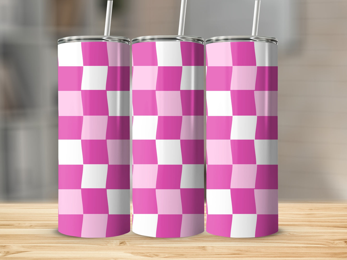 Three pink and white checkered tumblers with straws on a wooden surface.
