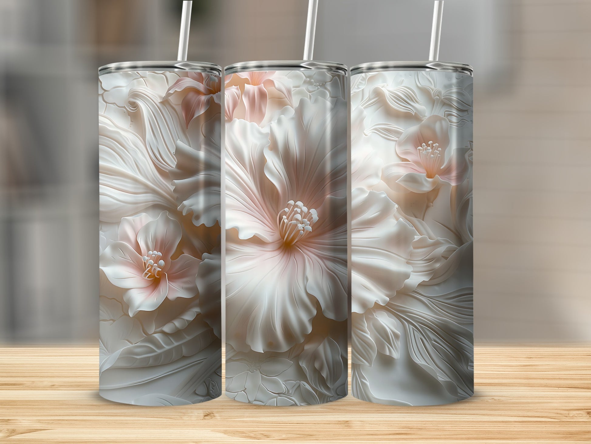 Three floral embossed tumblers with straws on a wooden surface.
