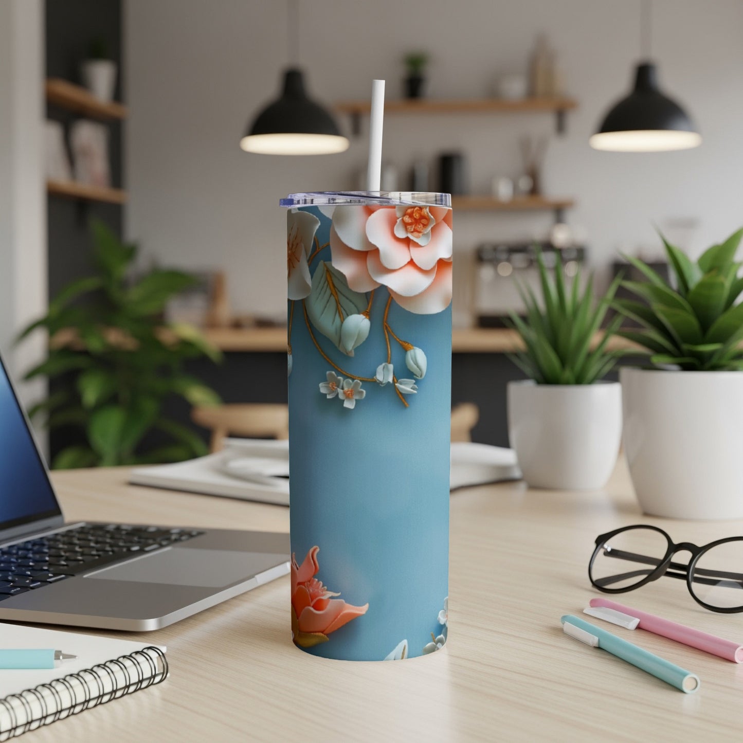 Blue tumbler with floral design on a desk next to a laptop.