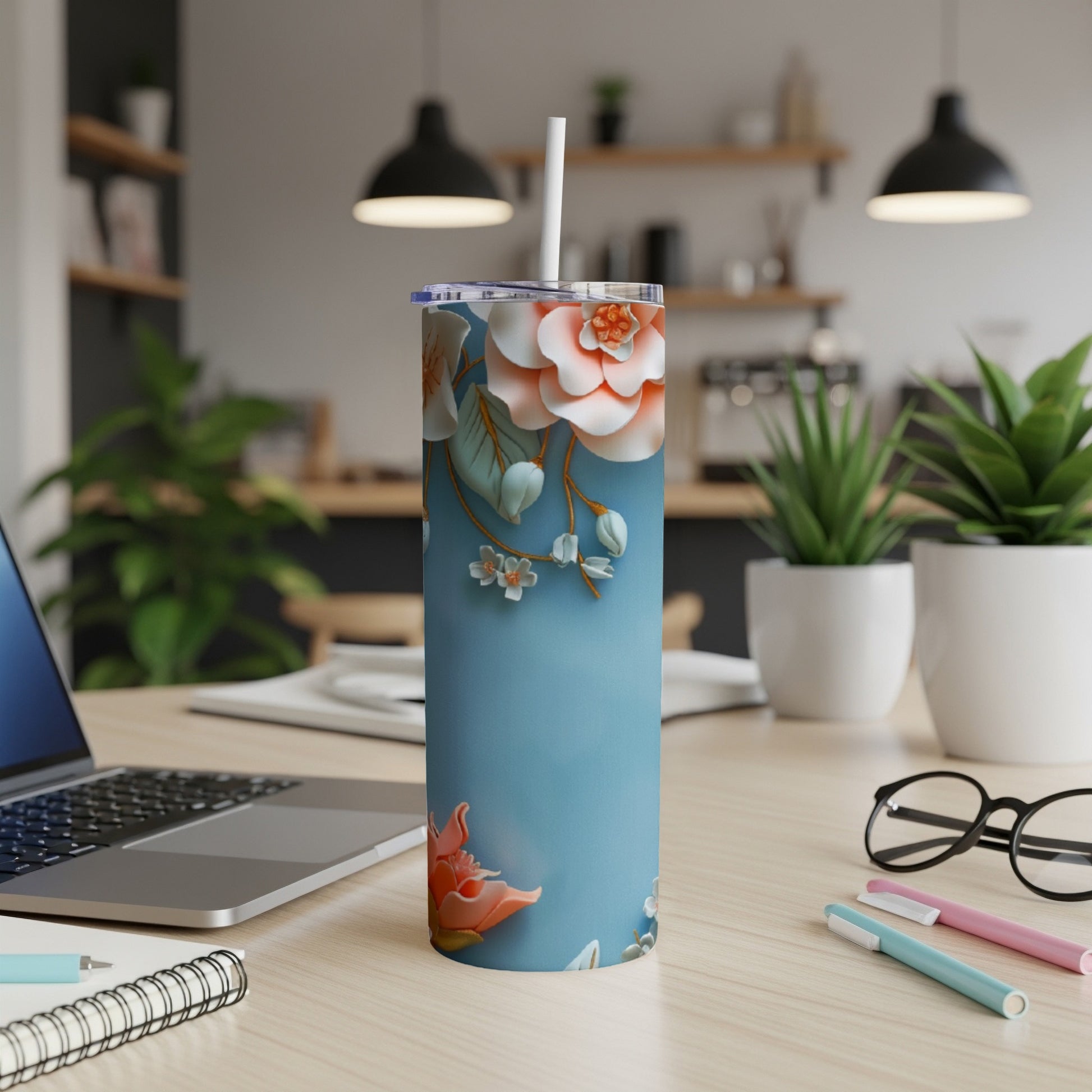 Blue tumbler with floral design on a desk next to a laptop.