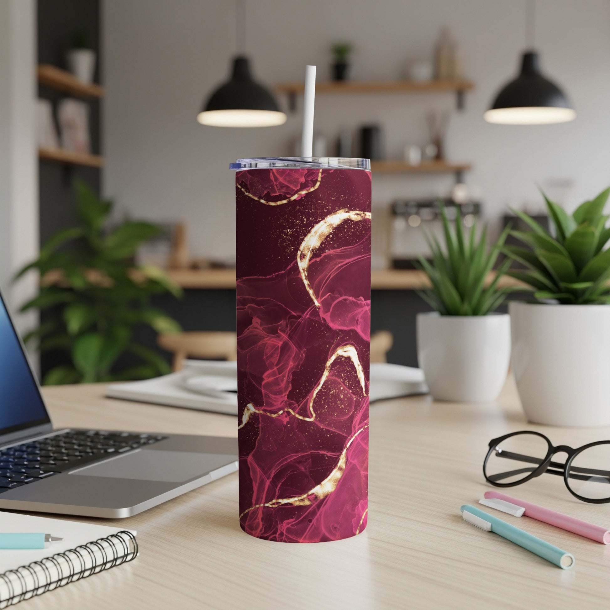 Maroon and gold abstract marble pattern tumbler with straw on a desk.