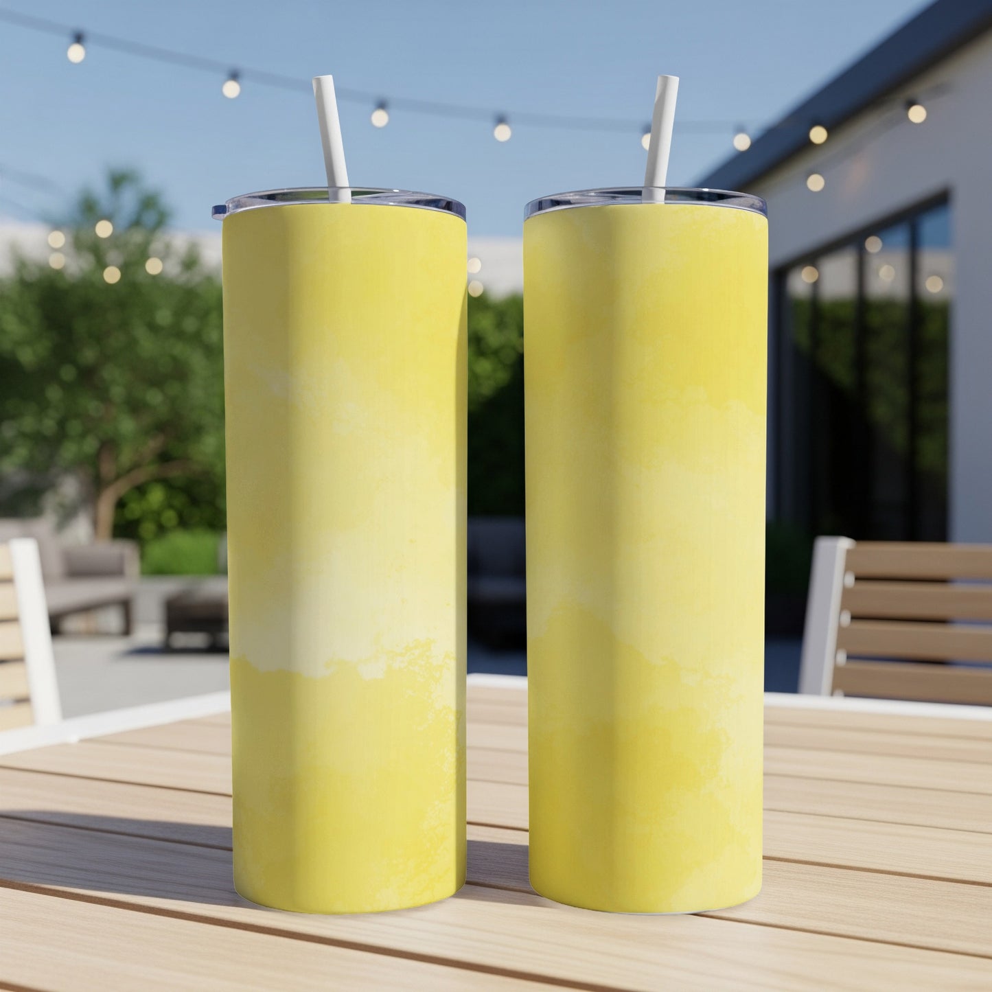 Two yellow tumblers with straws sit on a table outdoors.