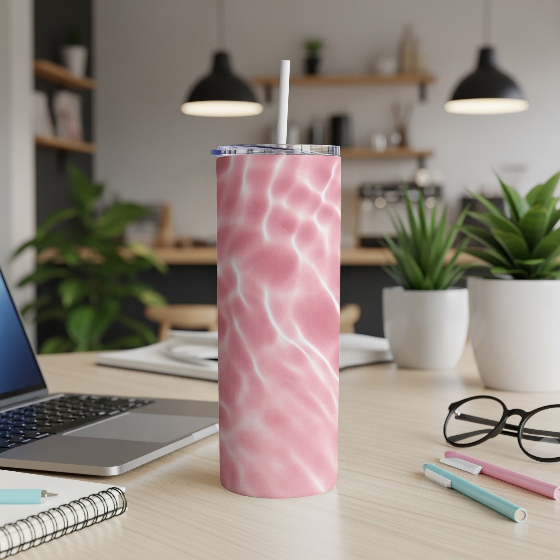 Pink marble tumbler with straw on desk with laptop and plants.