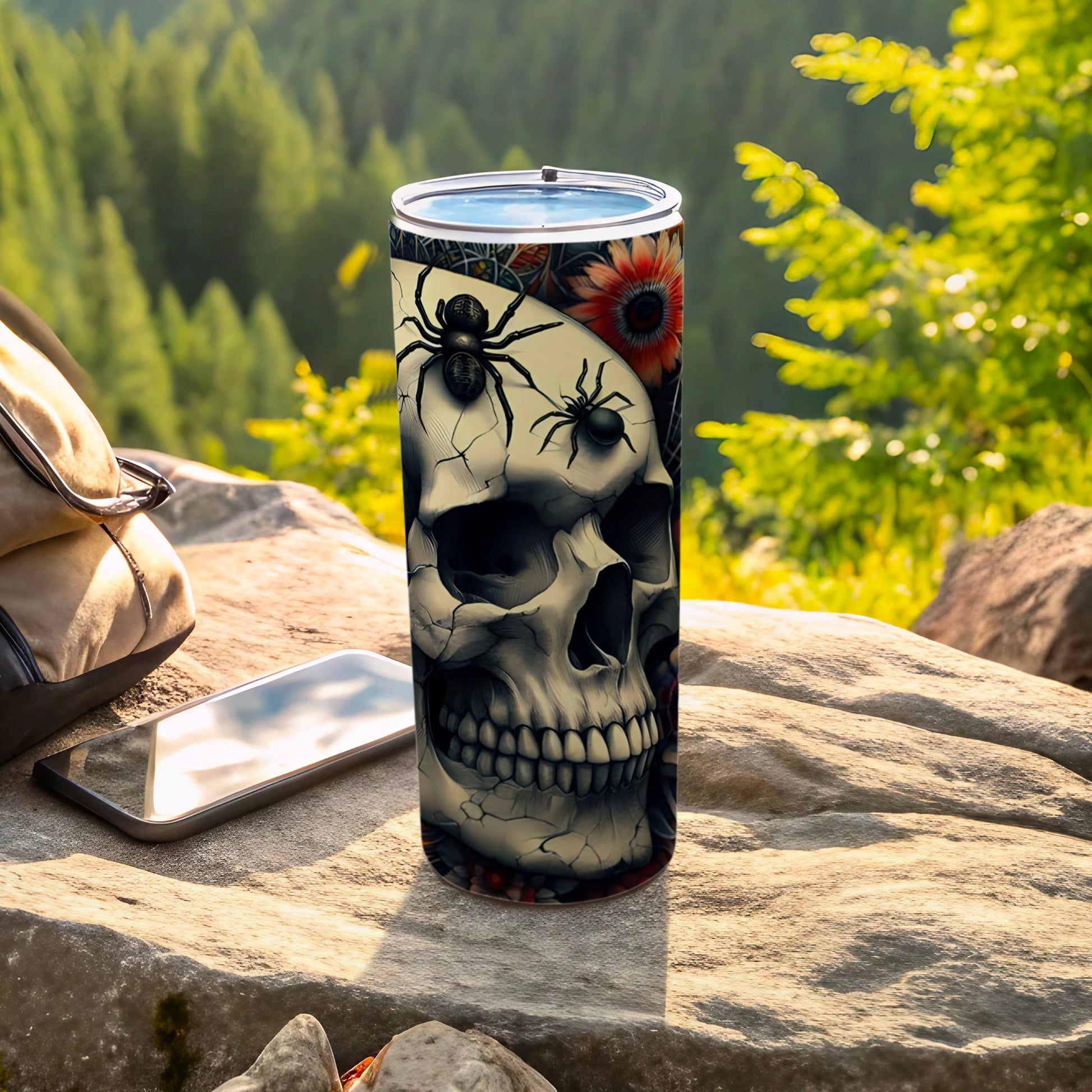 Tumbler with skull, spiders, and floral design on a rock.