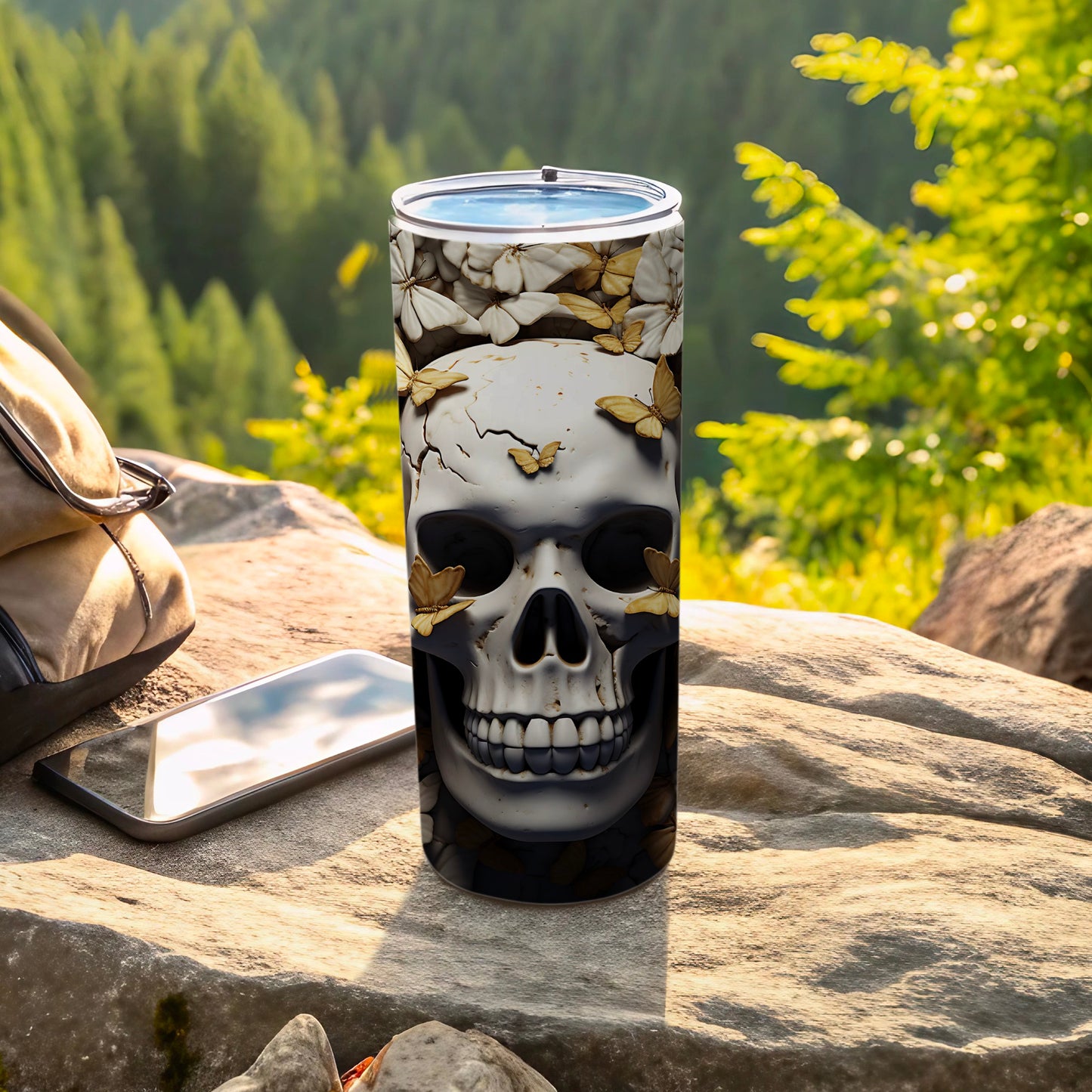 Skull and butterfly patterned tumbler on a rock with a backpack and phone.