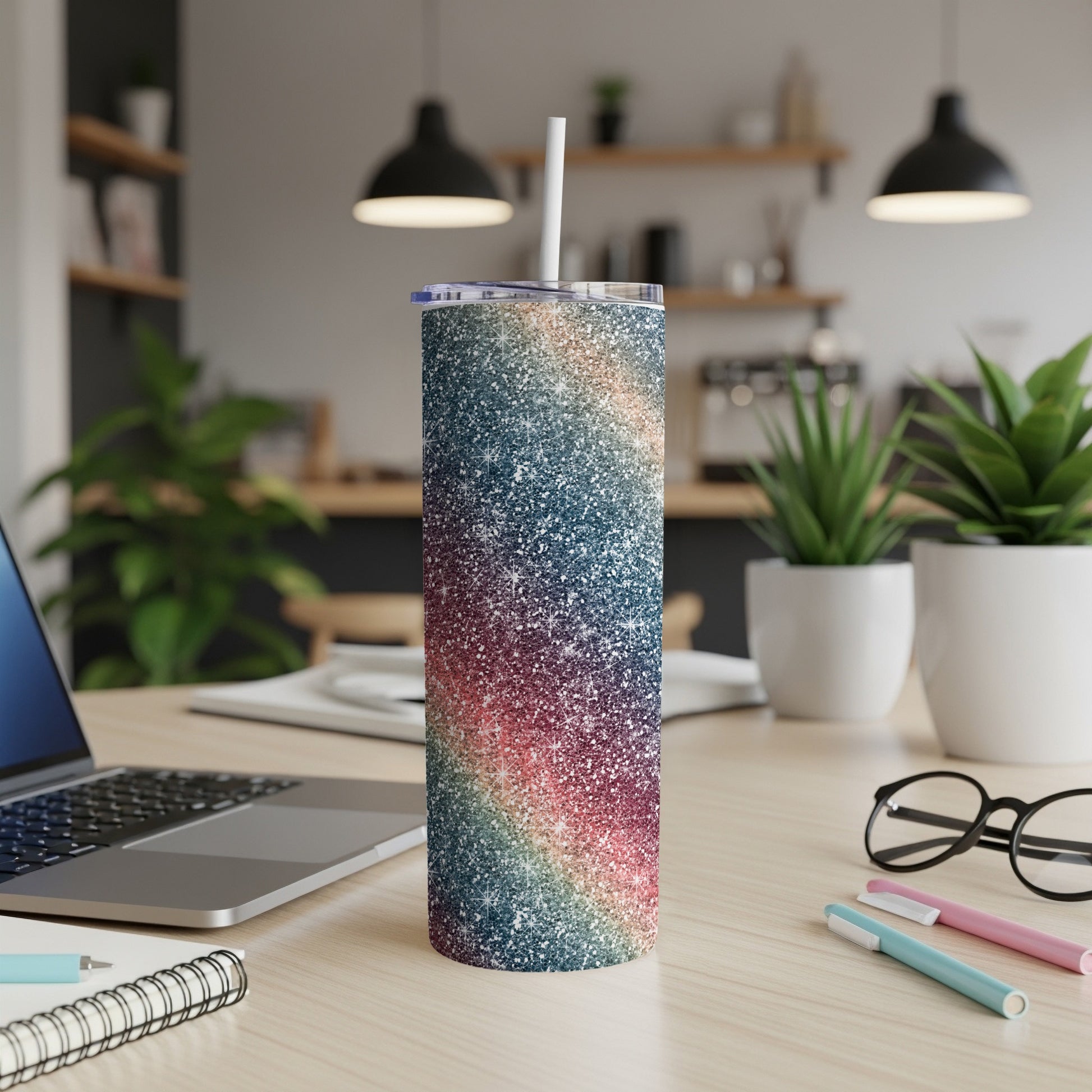 Glittery rainbow tumbler with straw on a desk beside a laptop and glasses.
