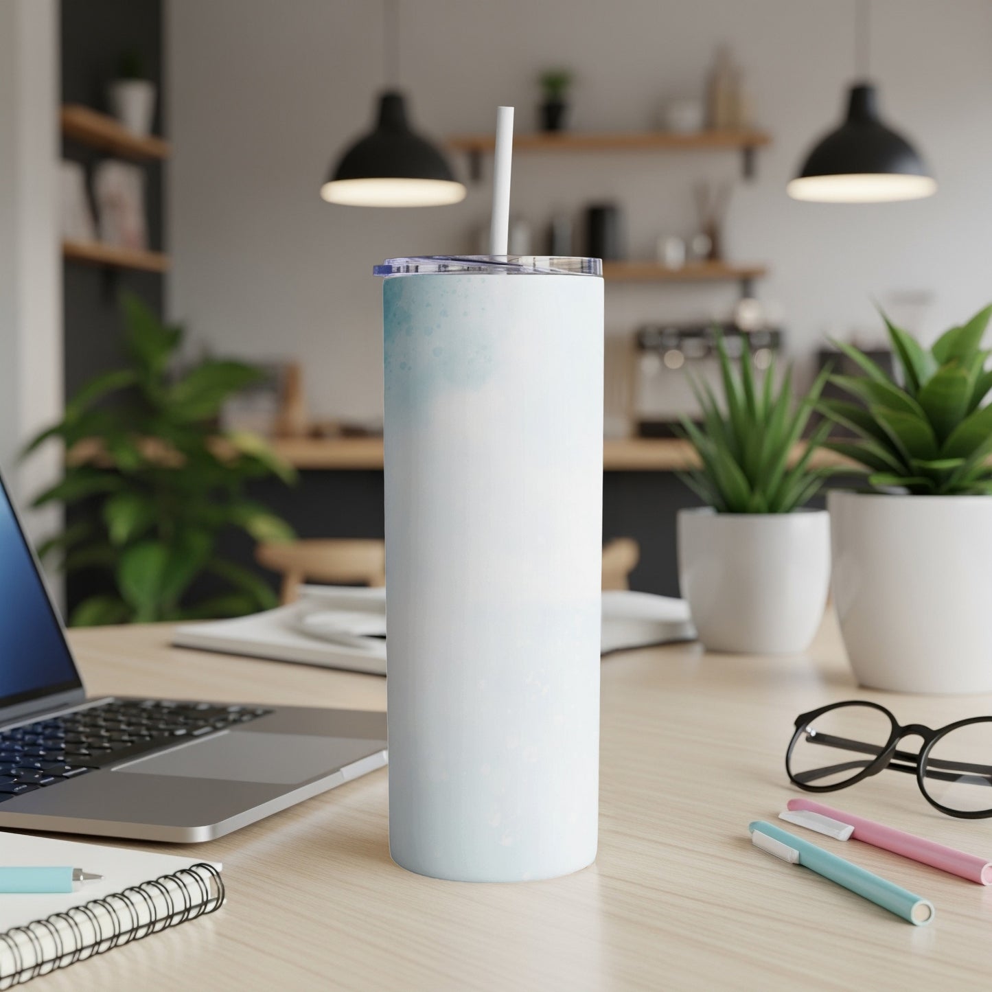 White tumbler with blue watercolor accents and a straw on a desk.