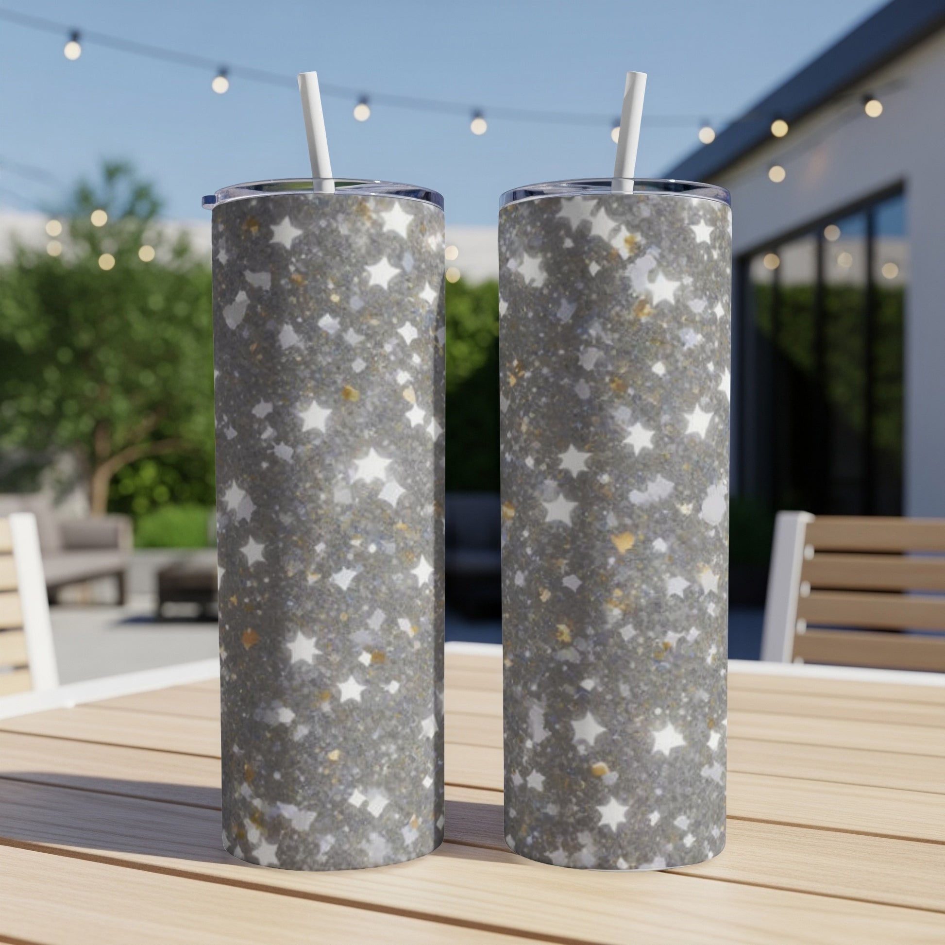 Two sparkly star-patterned tumblers with straws on a wooden table.