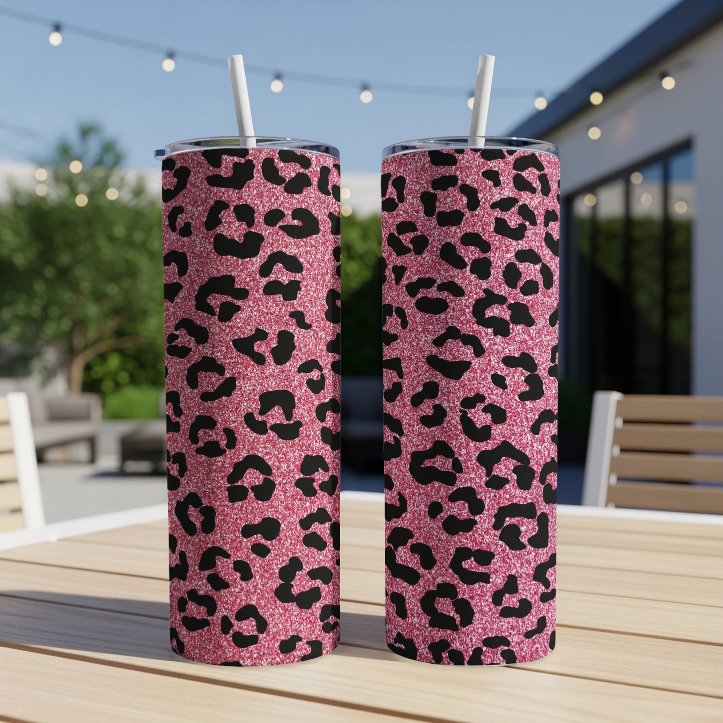Two pink glitter leopard print tumblers with straws on a wooden table.