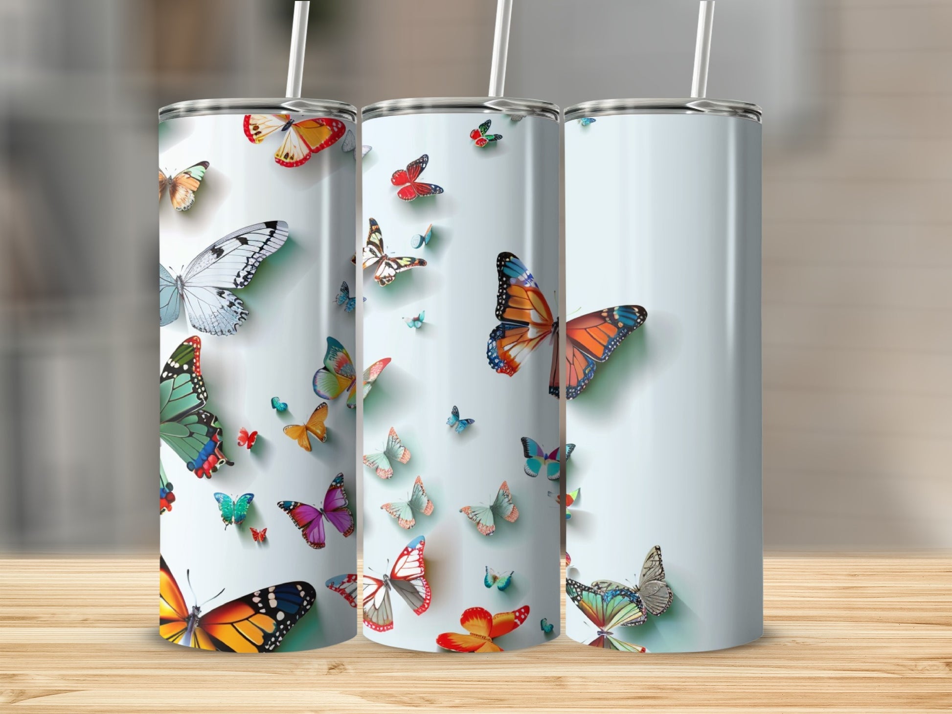 Three tumblers with colorful butterfly designs on a wooden surface.