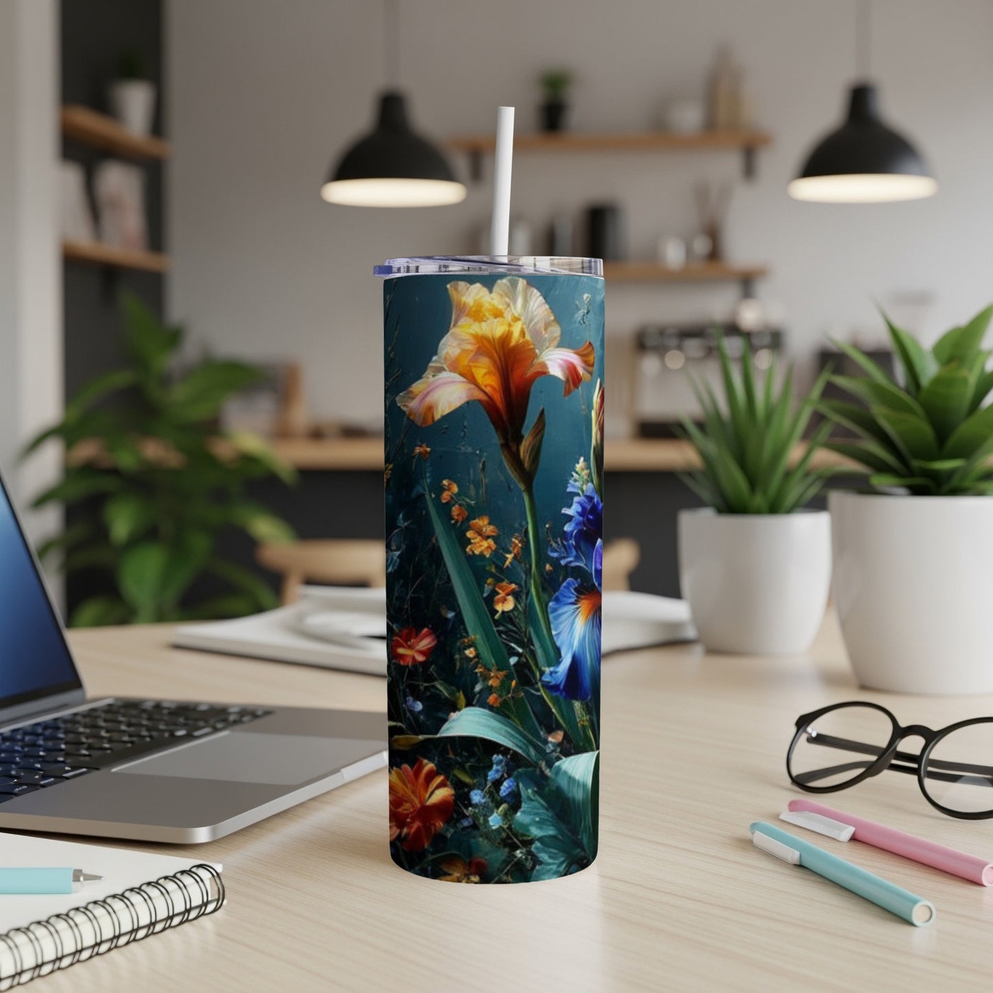 Tumbler with colorful floral design on a desk with laptop and pens.