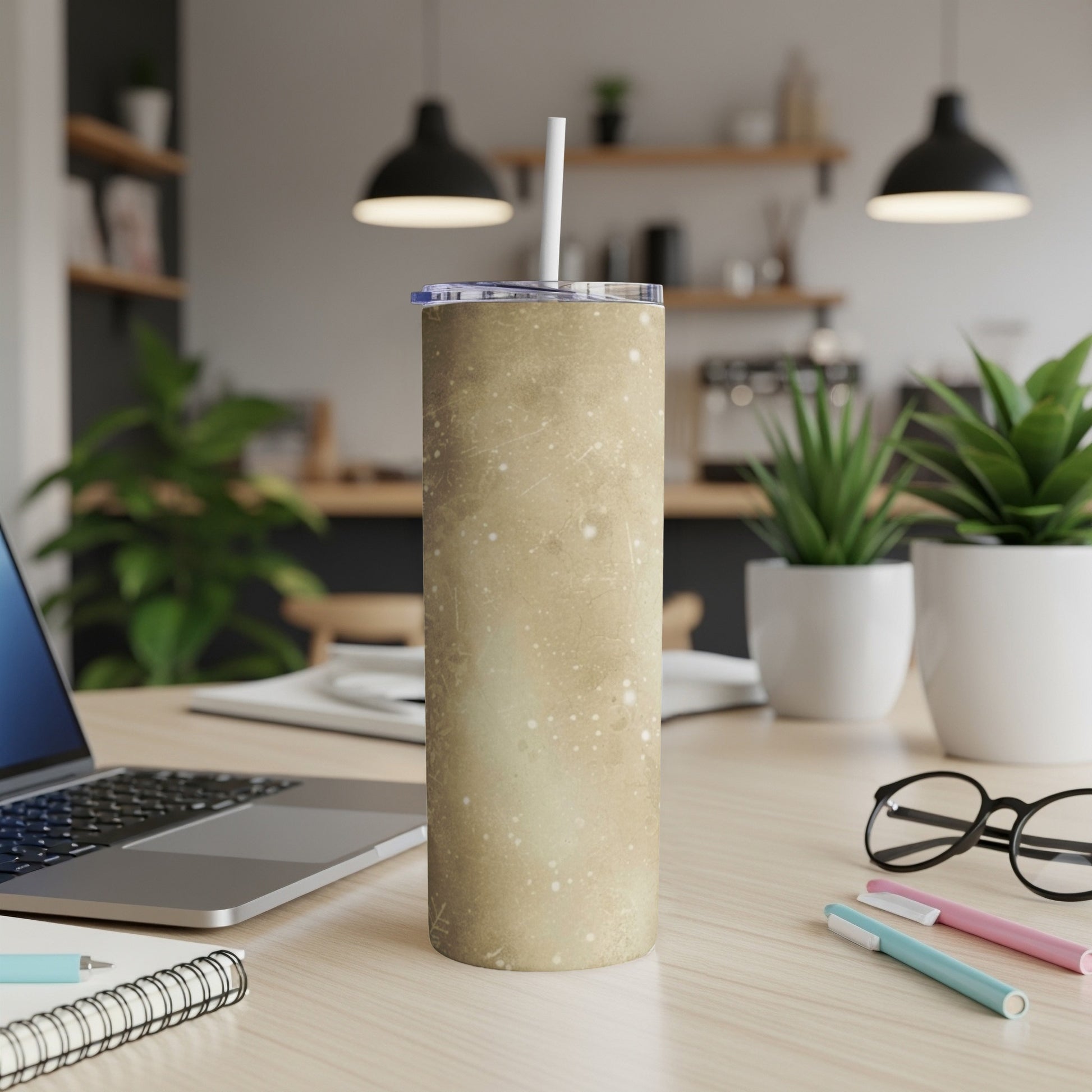 Tan speckled tumbler with straw on a desk with laptop and pens.