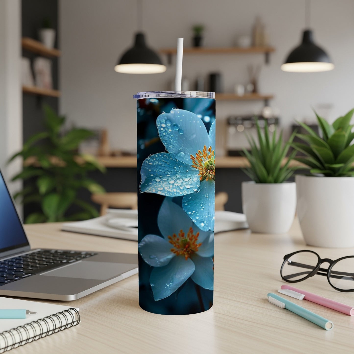 Blue flowers with water droplets on a white tumbler, with office supplies.