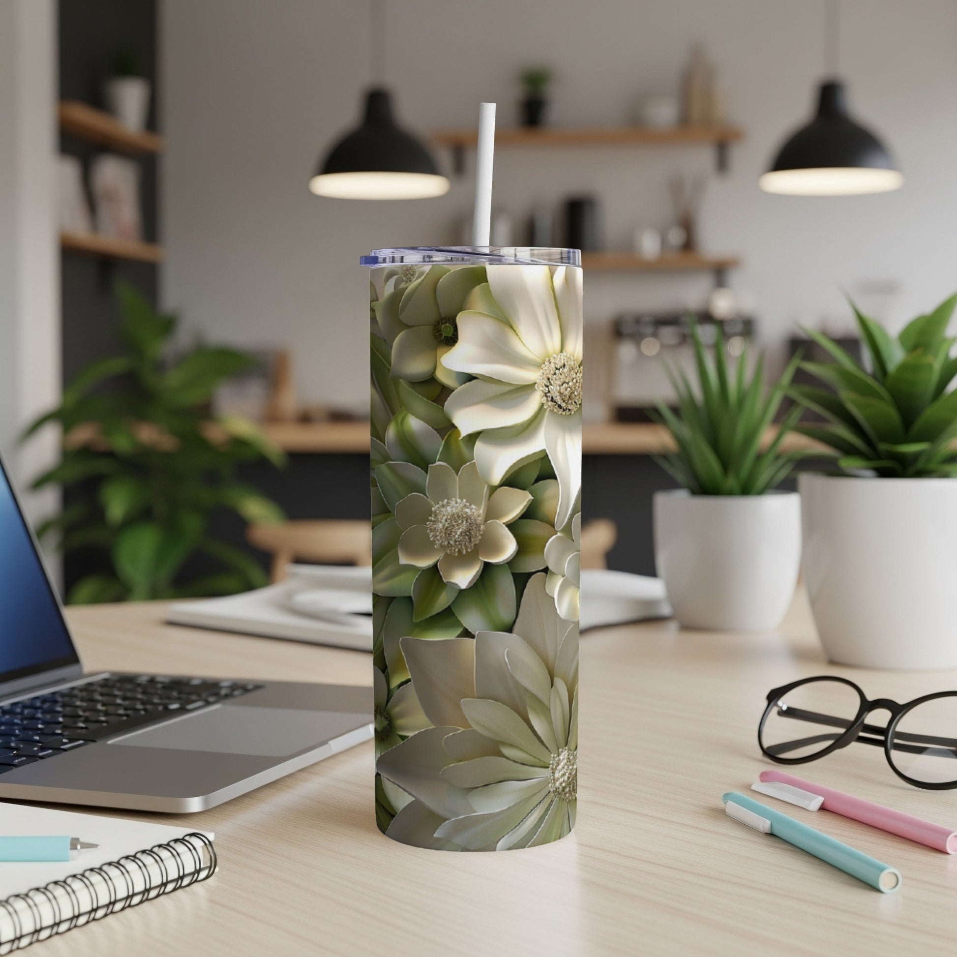 White and green floral patterned tumbler with straw on desk.