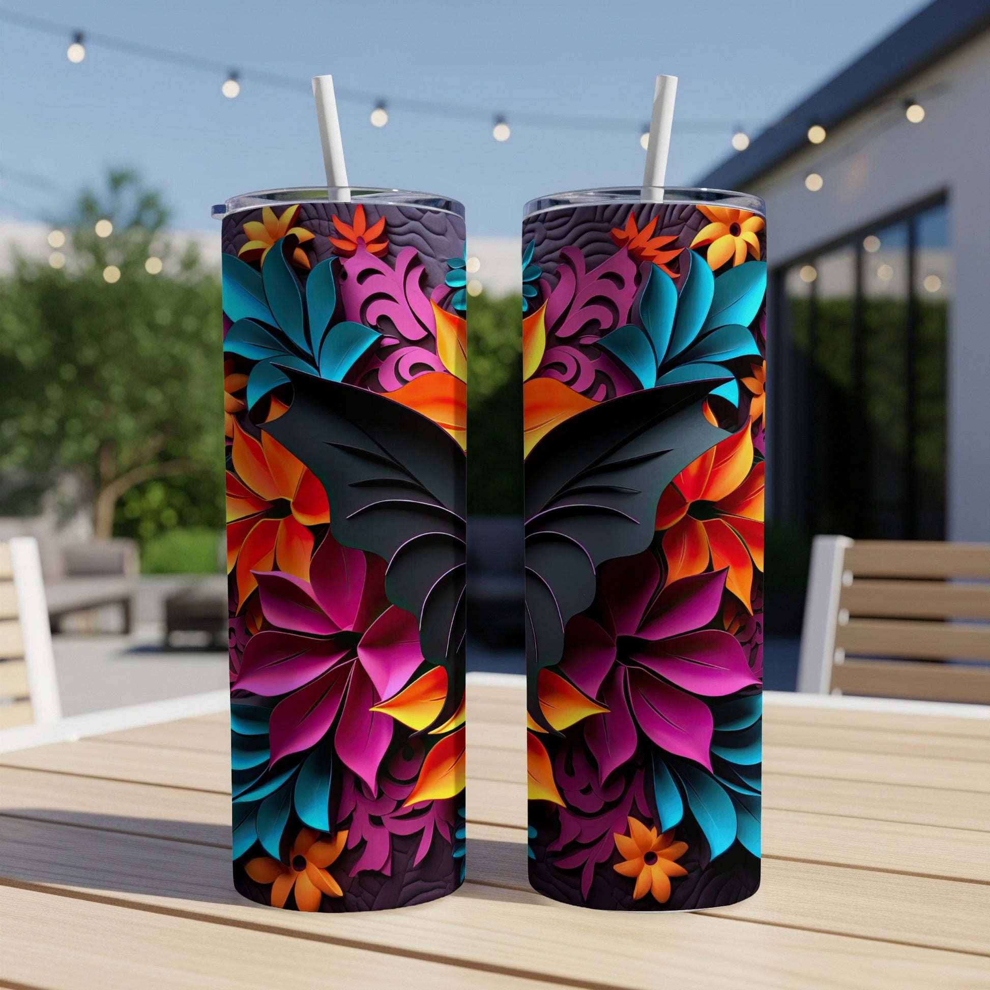 Two tumblers with vibrant floral and butterfly wing designs on a wooden table outdoors.