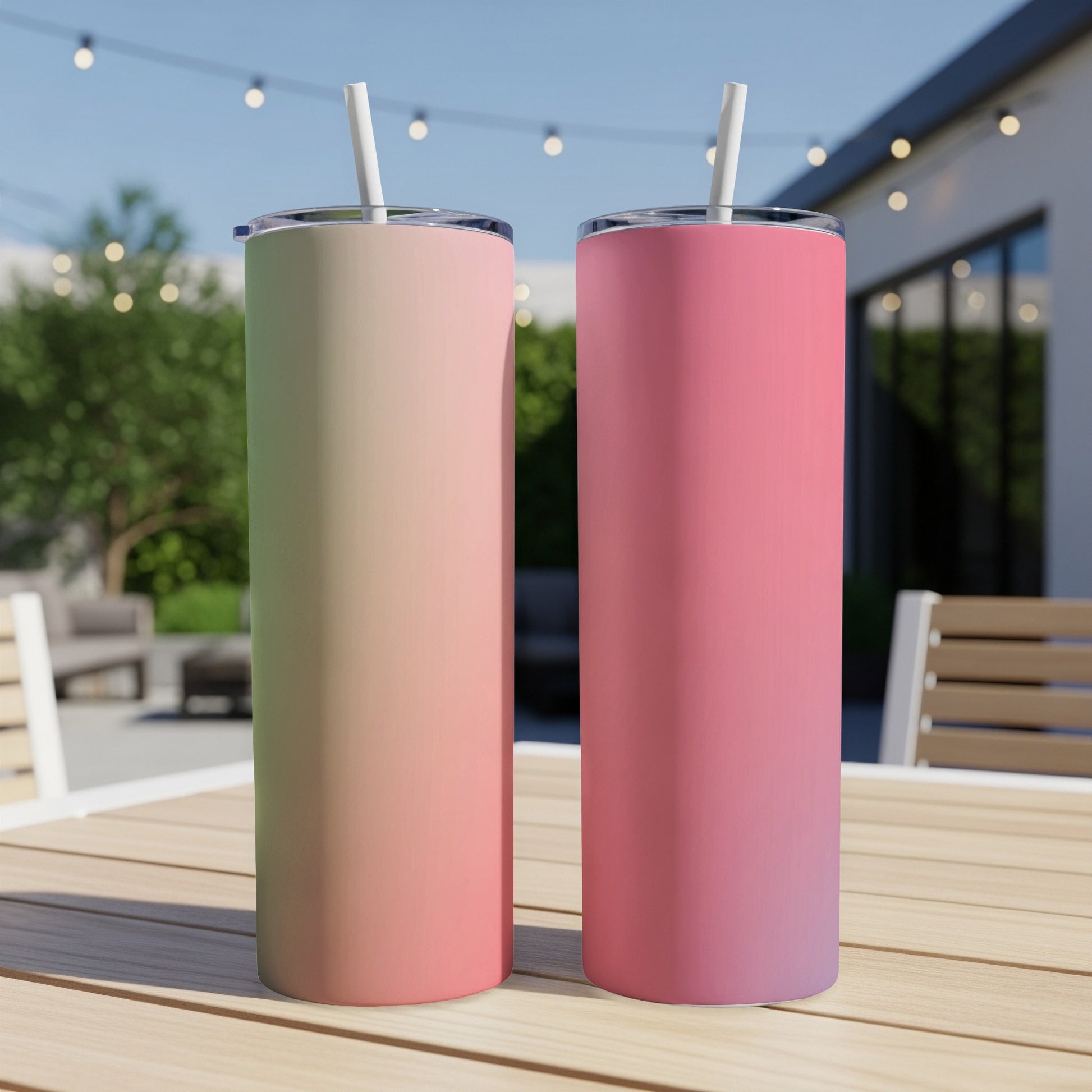 Two tall, skinny tumblers with straws are displayed on a wooden table outdoors.