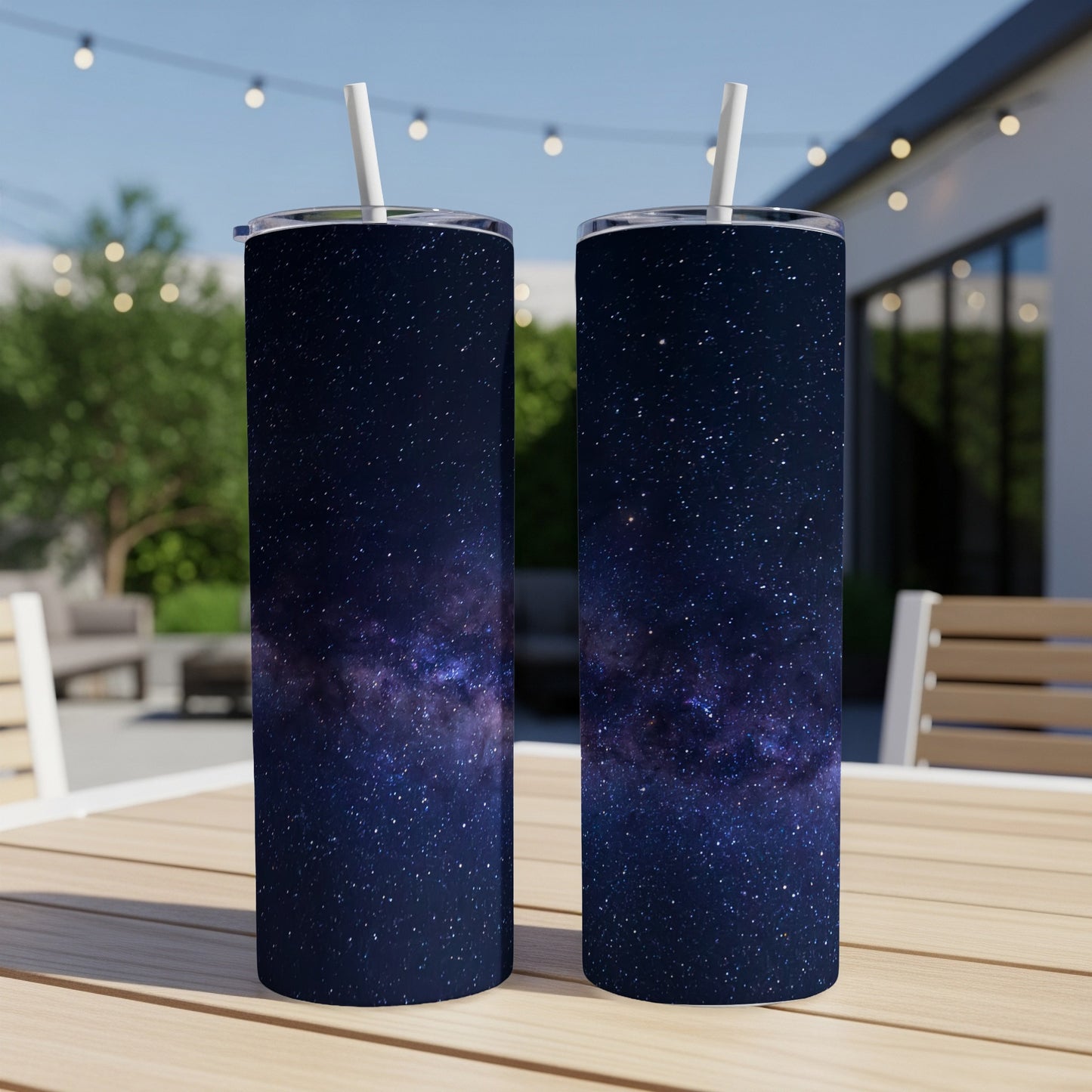 Two tumblers with a starry night sky design sit on a wooden table outdoors.