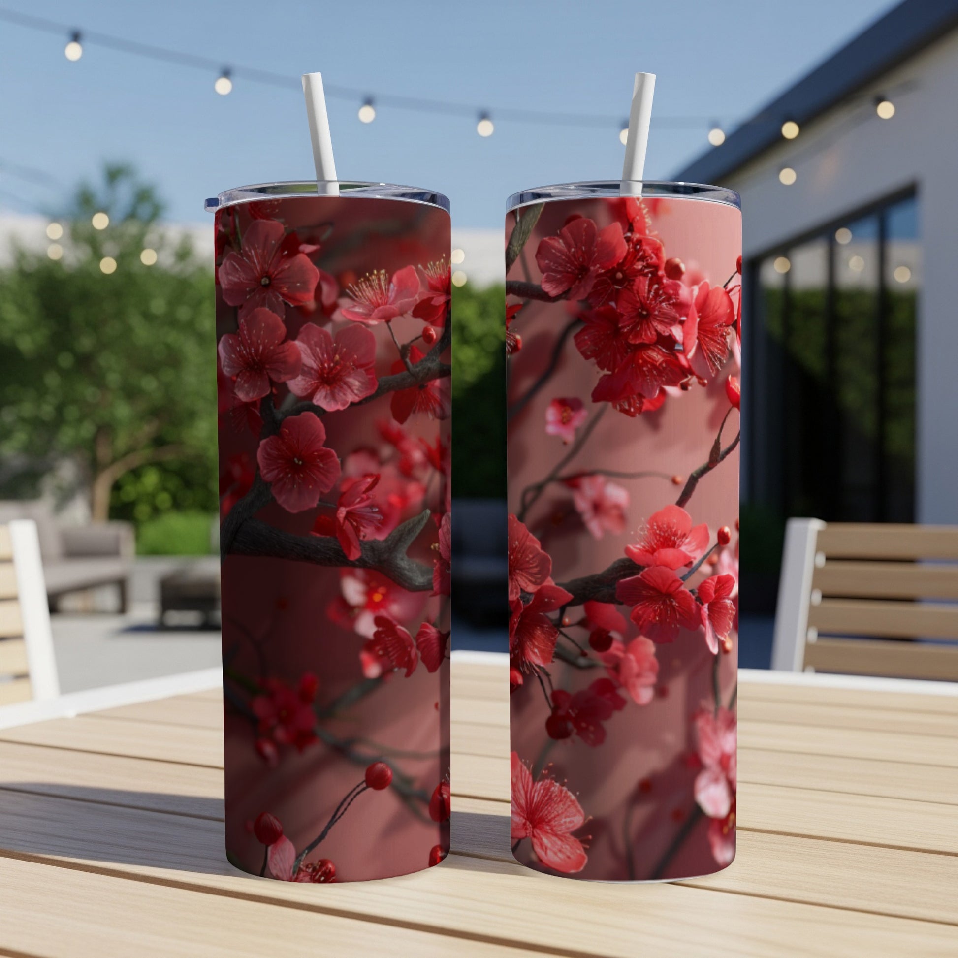 Two tumblers with red cherry blossoms on a table outdoors.