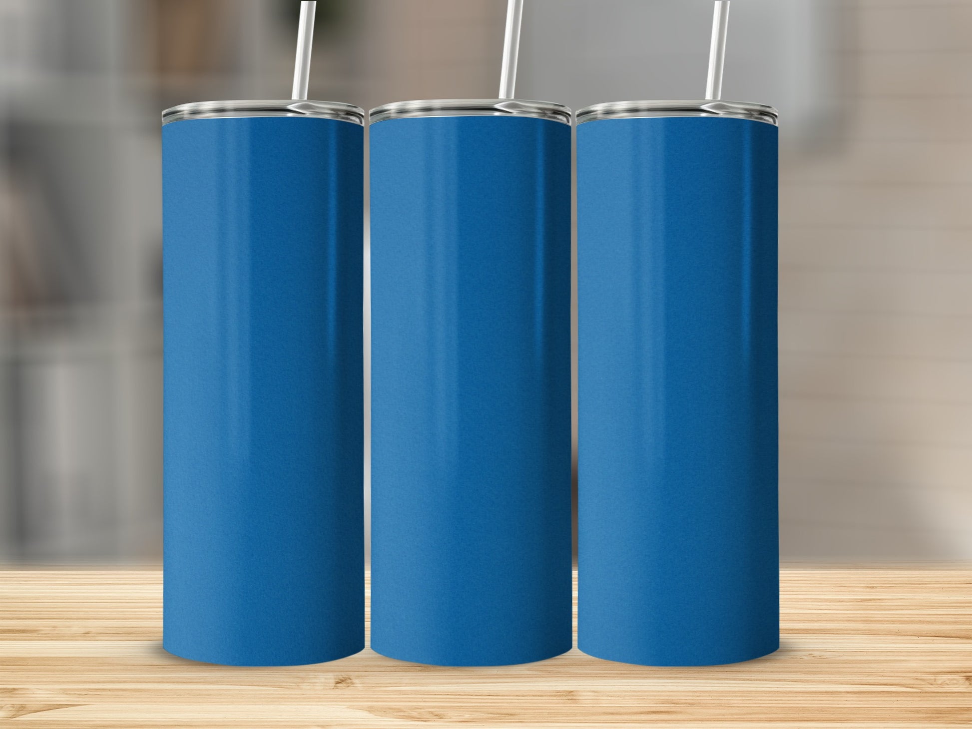 Three blue tumblers with white straws stand on a wooden surface.