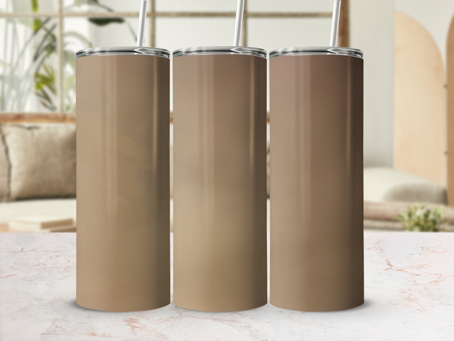 Three blank tan tumblers with straws stand on a marble surface.