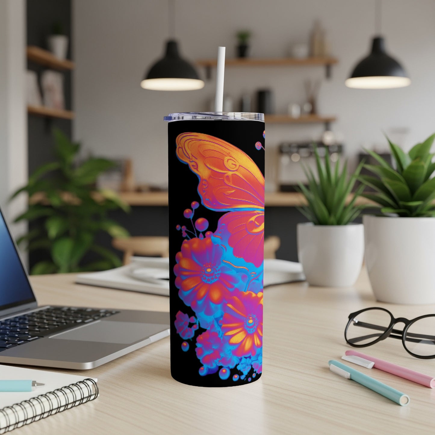 Black tumbler with colorful butterfly and floral design, on a desk.