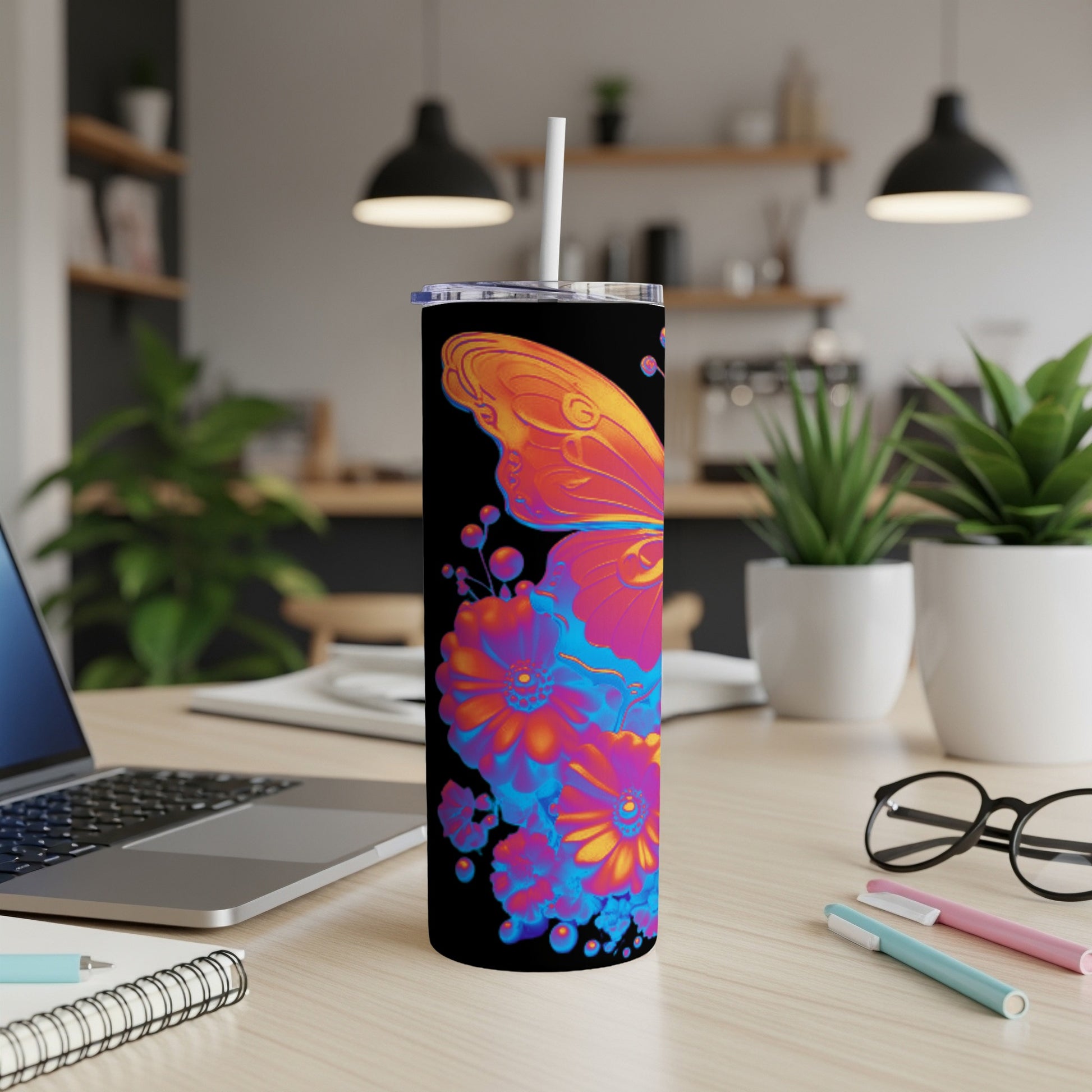 Black tumbler with colorful butterfly and floral design, on a desk.