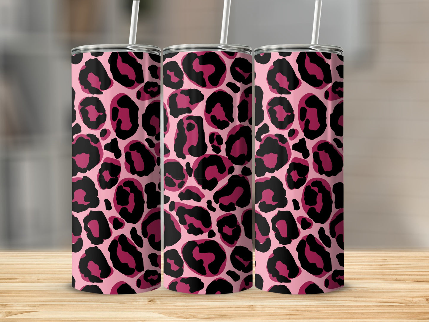Three pink tumblers with black and magenta leopard print design and white straws on a wooden surface.