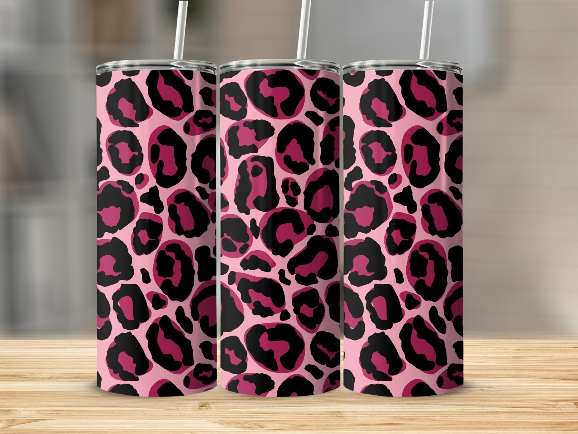 Three pink tumblers with black and magenta leopard print design and white straws on a wooden surface.