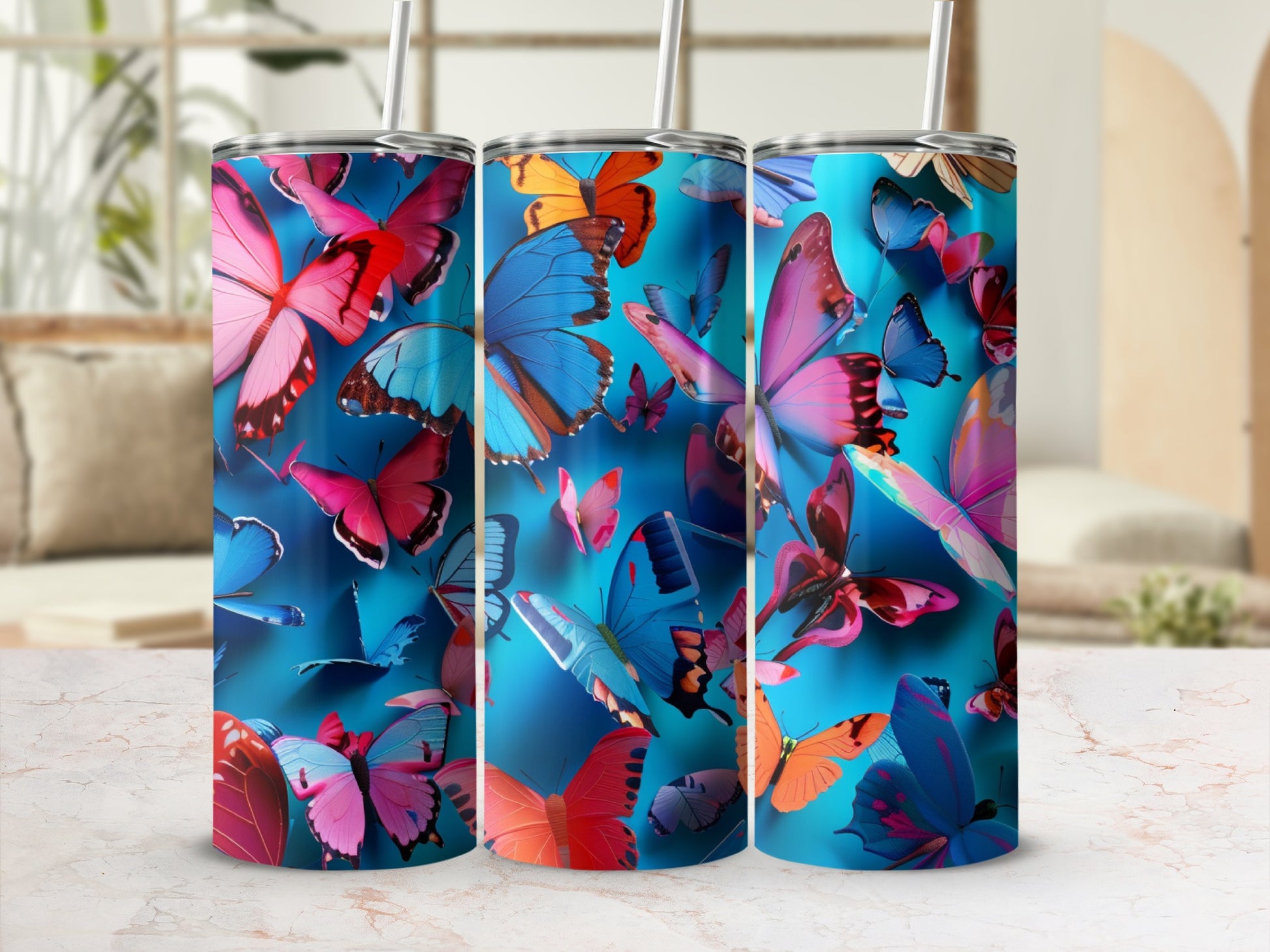 Three tall tumblers with a vibrant butterfly pattern on a light marbled surface.