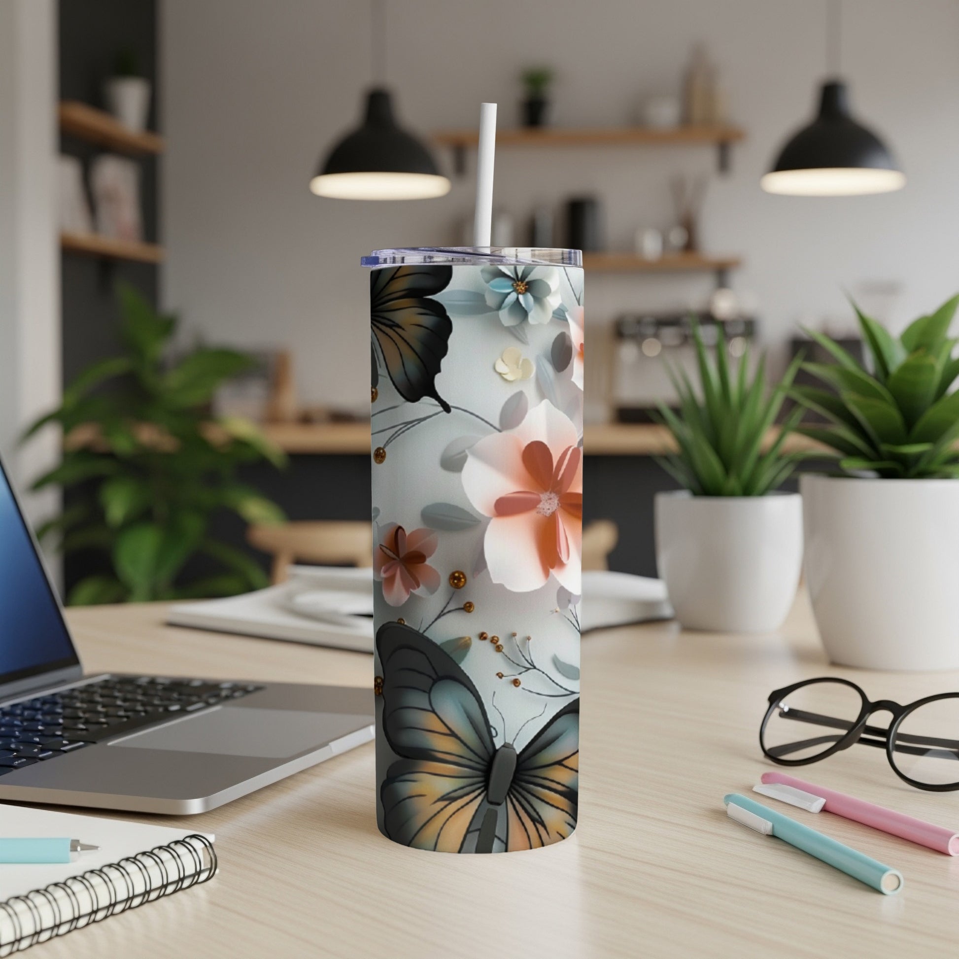 Floral and butterfly patterned tumbler with a white straw on a desk.