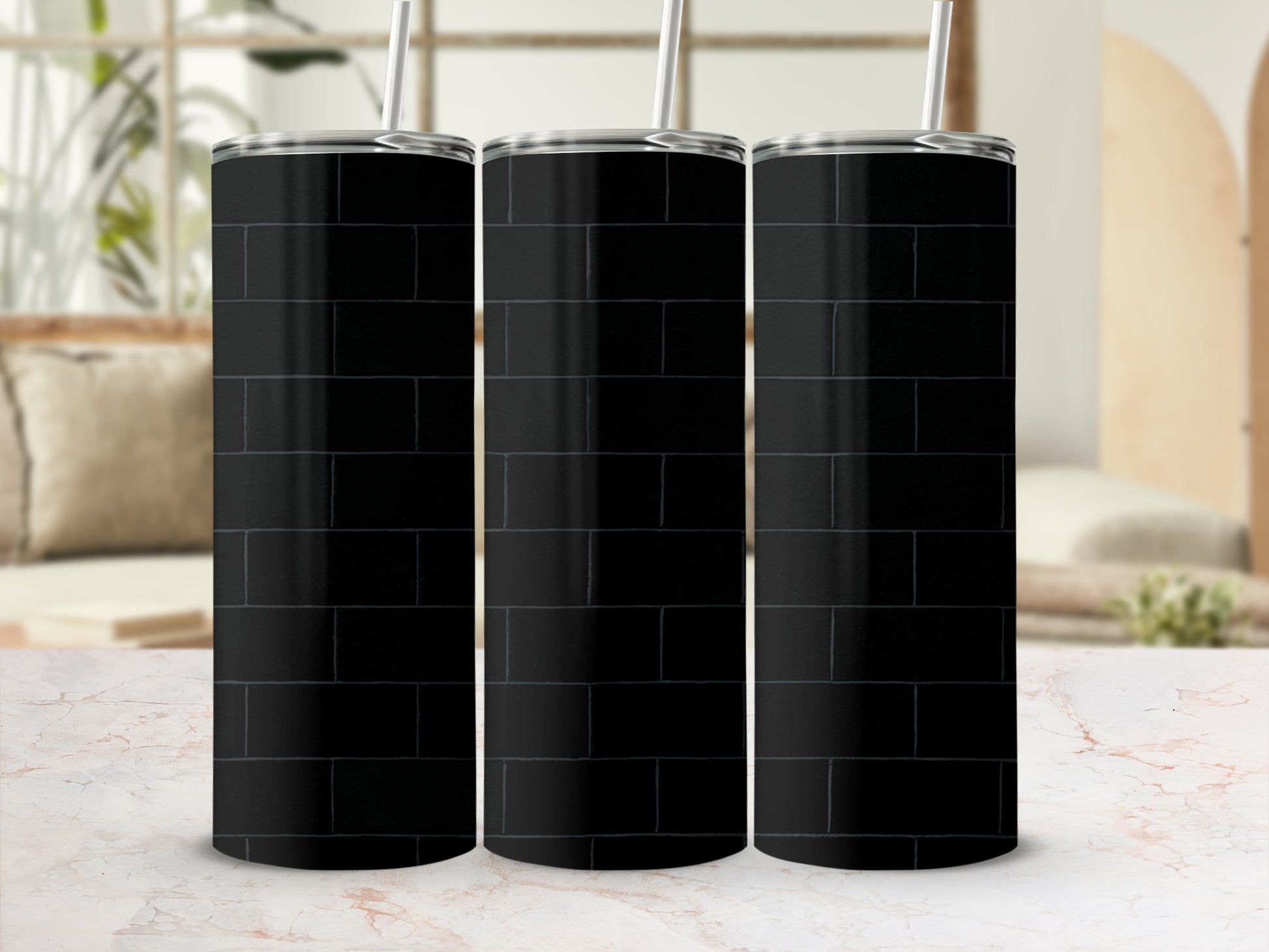 Three black brick pattern tumblers with straws on a marble surface.