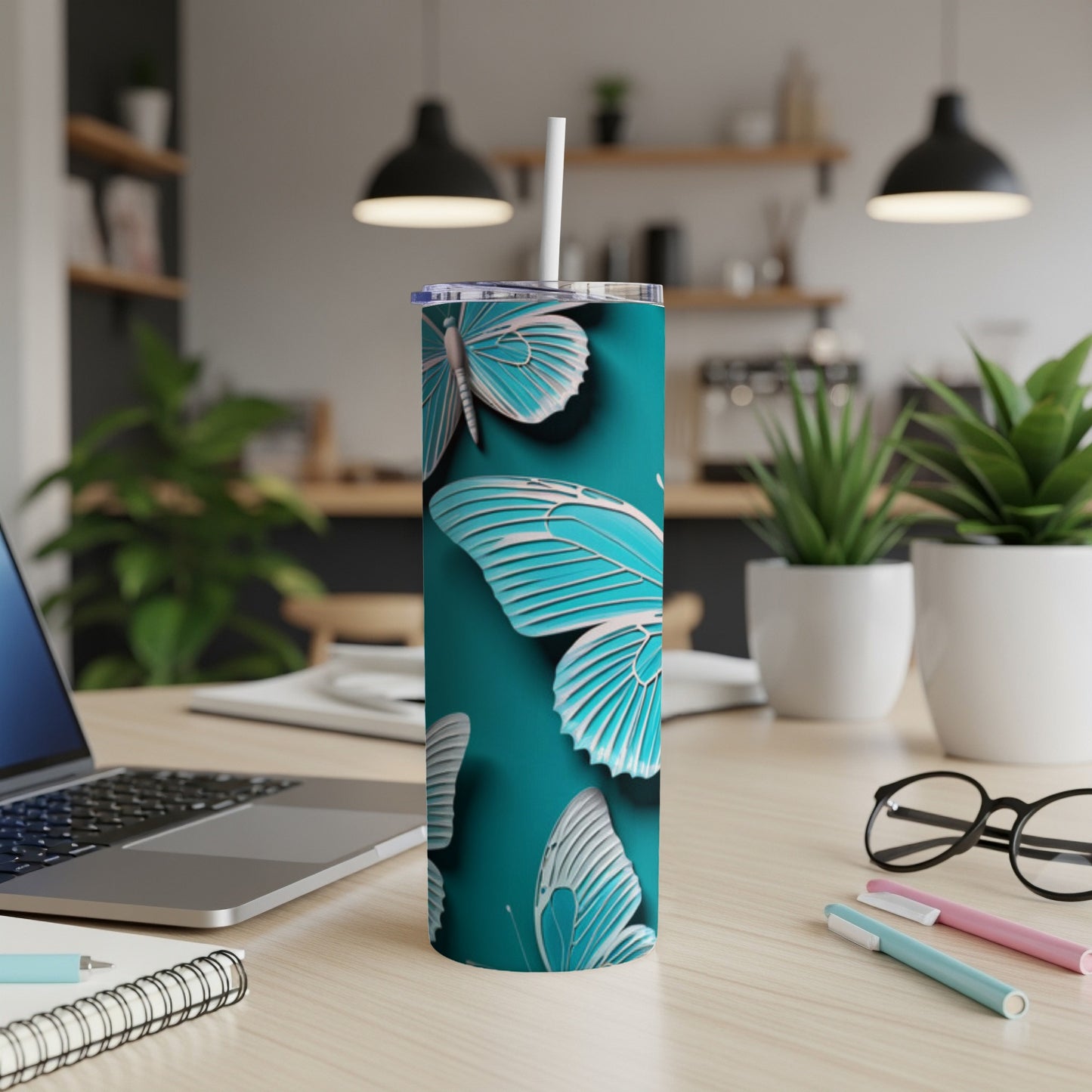Turquoise tumbler with white butterfly pattern and straw on desk.