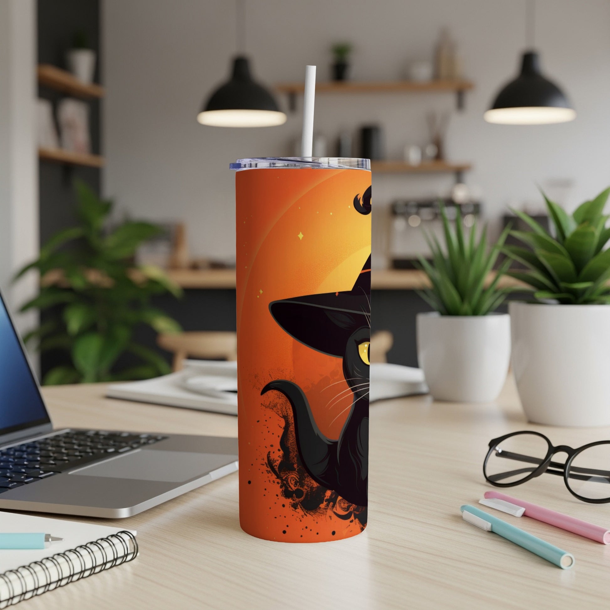 Orange tumbler with black cat wearing witch hat, straw, on a desk.
