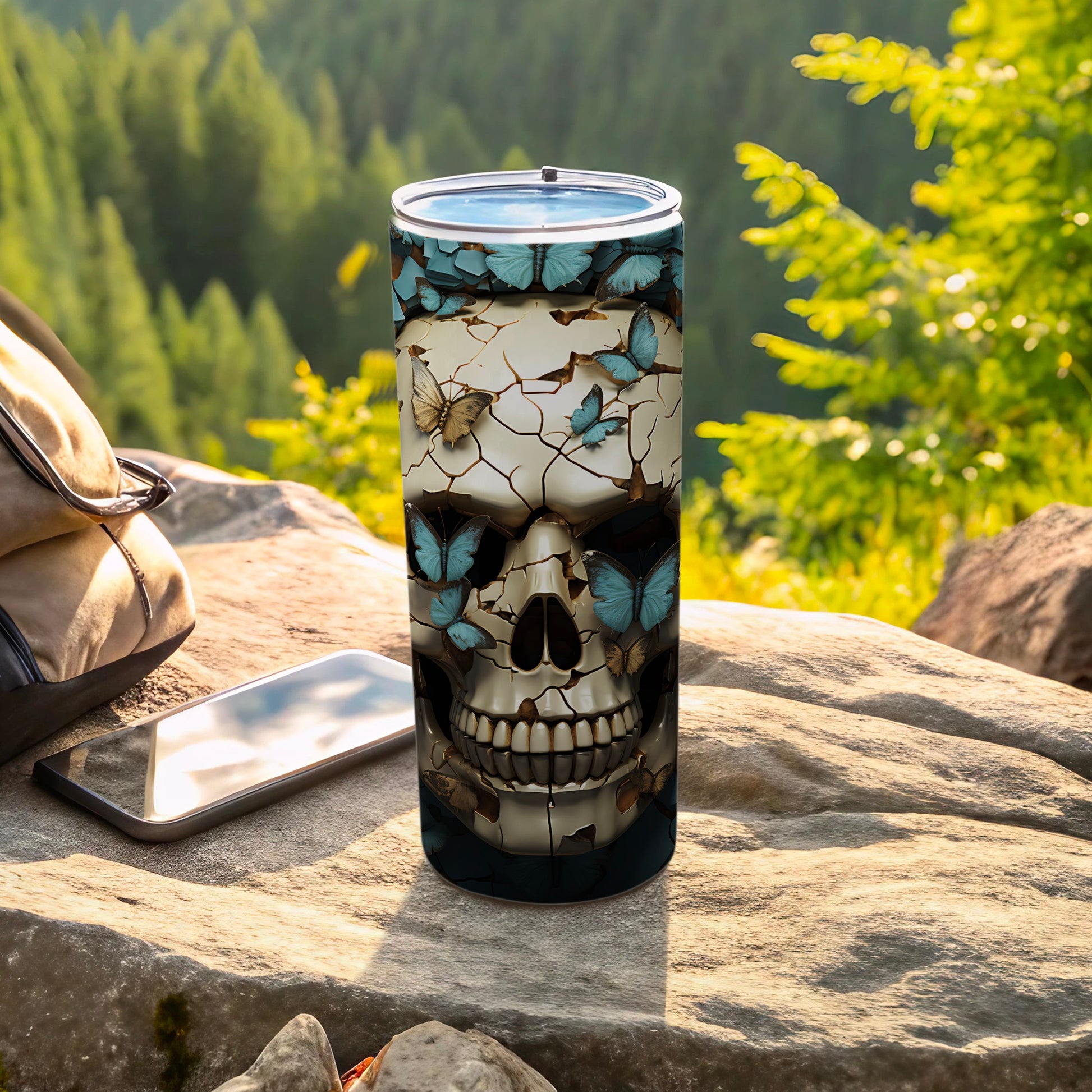 Skull and butterfly design on a tall tumbler beside a backpack and phone.