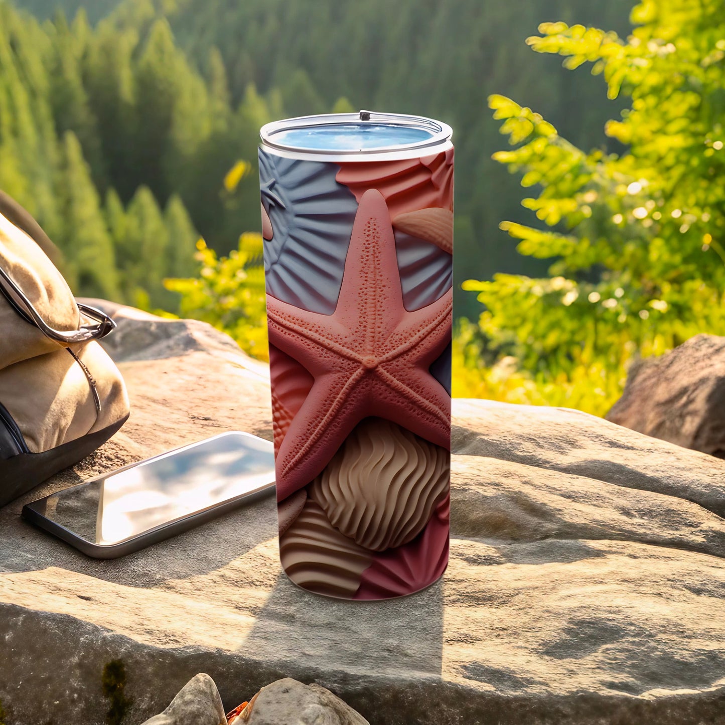 Tall tumbler with starfish and seashell pattern, resting on rocks outdoors.