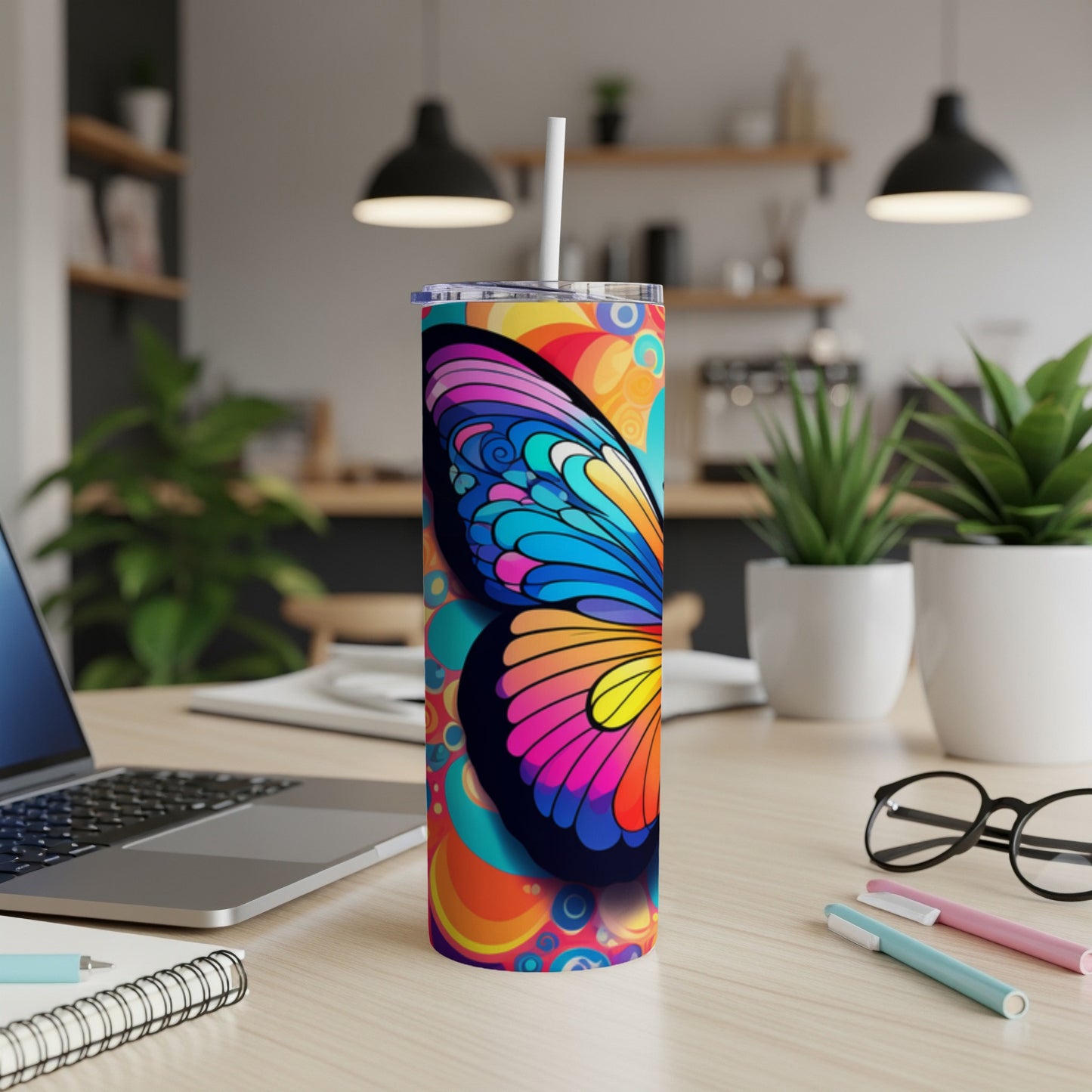 Colorful butterfly tumbler with a straw on a desk with a laptop.