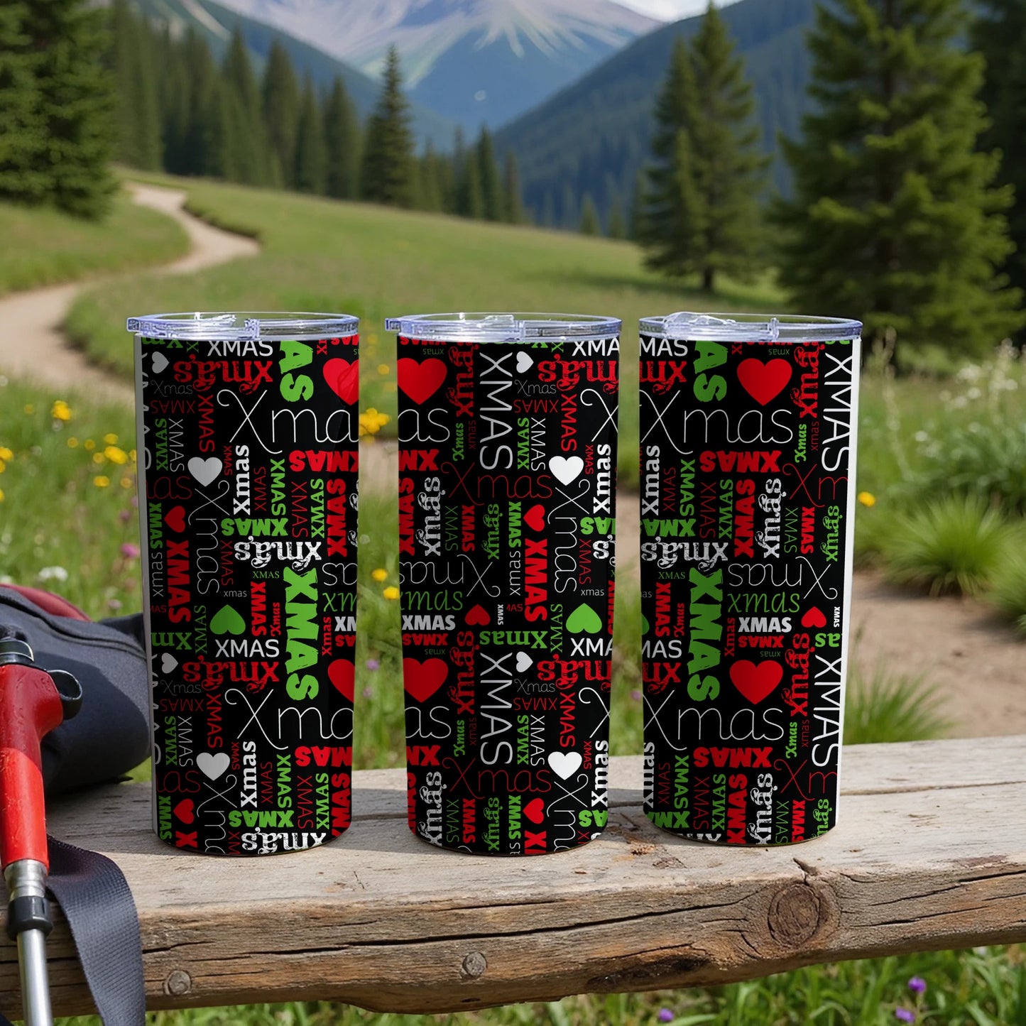 Three tumblers with repeating "XMAS" pattern on wooden surface with blurred nature background.