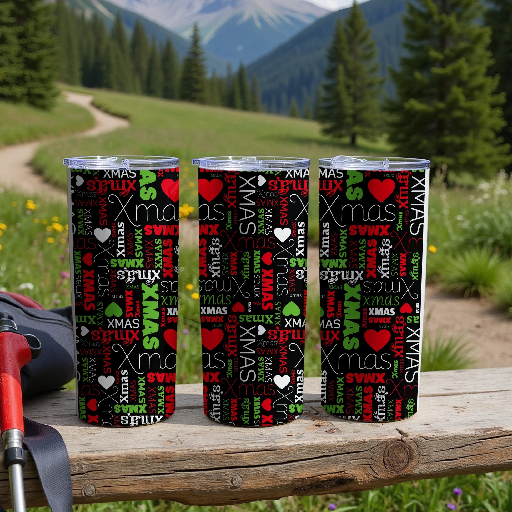 Three tumblers with repeating "XMAS" pattern on wooden surface with blurred nature background.
